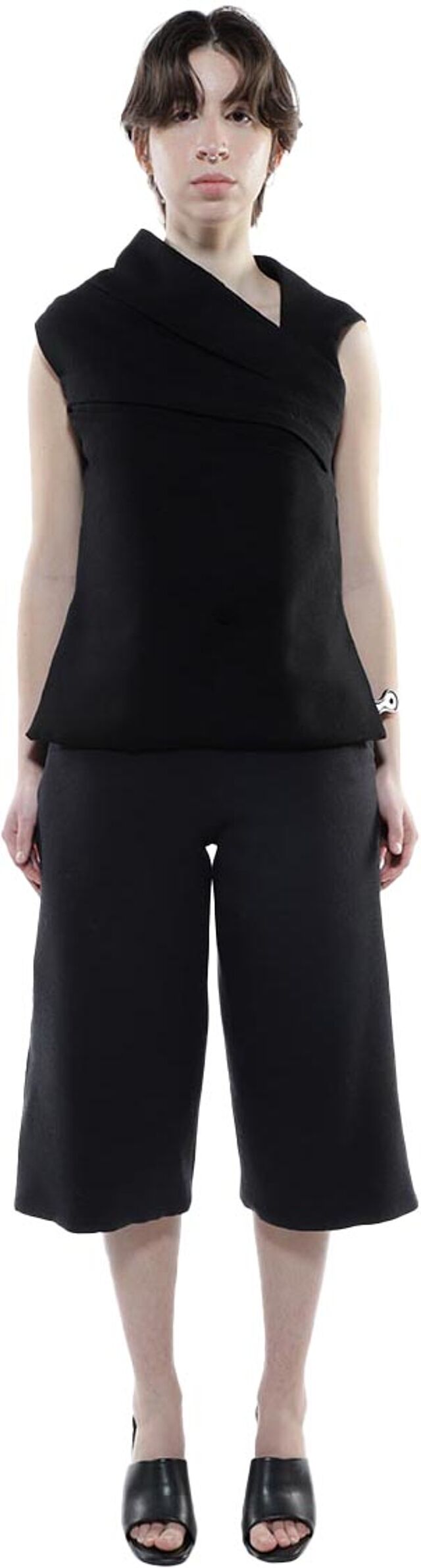 A woman with short brown hair is shown from the knees up wearing a black sleeveless top and culottes, and black open-toe shoes.