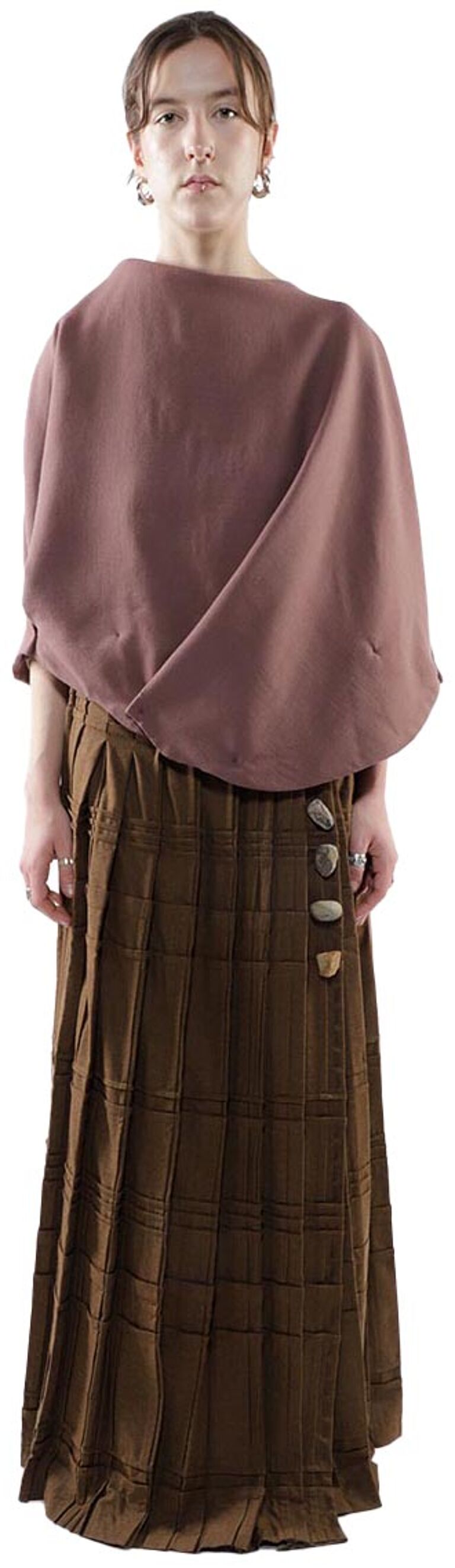 A woman with light skin and brown hair is wearing a mauve, loose-fitting top and a brown pleated maxi skirt with a stone-embellished belt.