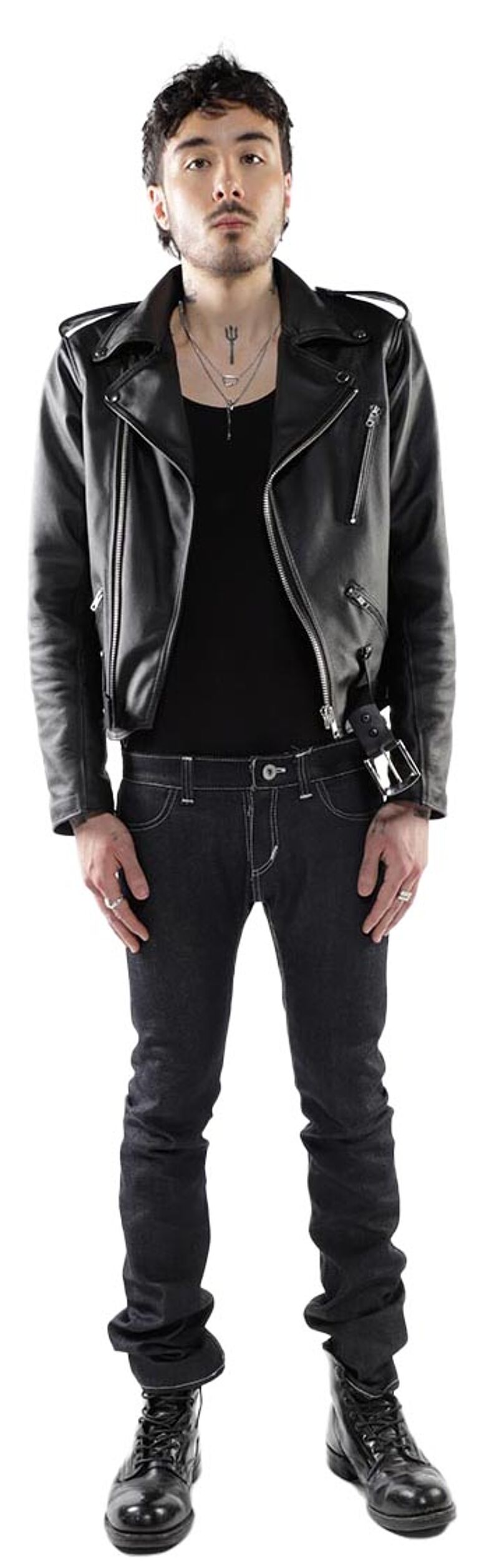 A young man with dark hair and a black leather jacket stands against a white background, wearing dark jeans and black combat boots.