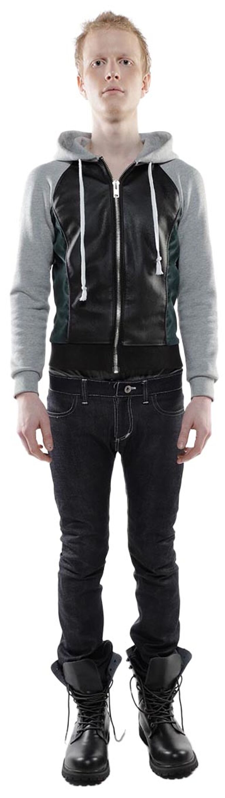 A young, fair-skinned man with short, light brown hair is standing against a white background wearing a gray and black hooded jacket, dark wash jeans, and black combat boots.