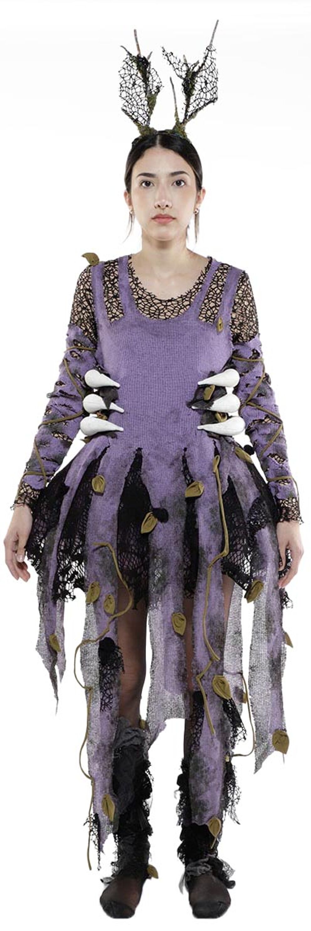 A woman in a purple and black tattered dress with antlers on her head and distressed leg warmers poses for the camera.