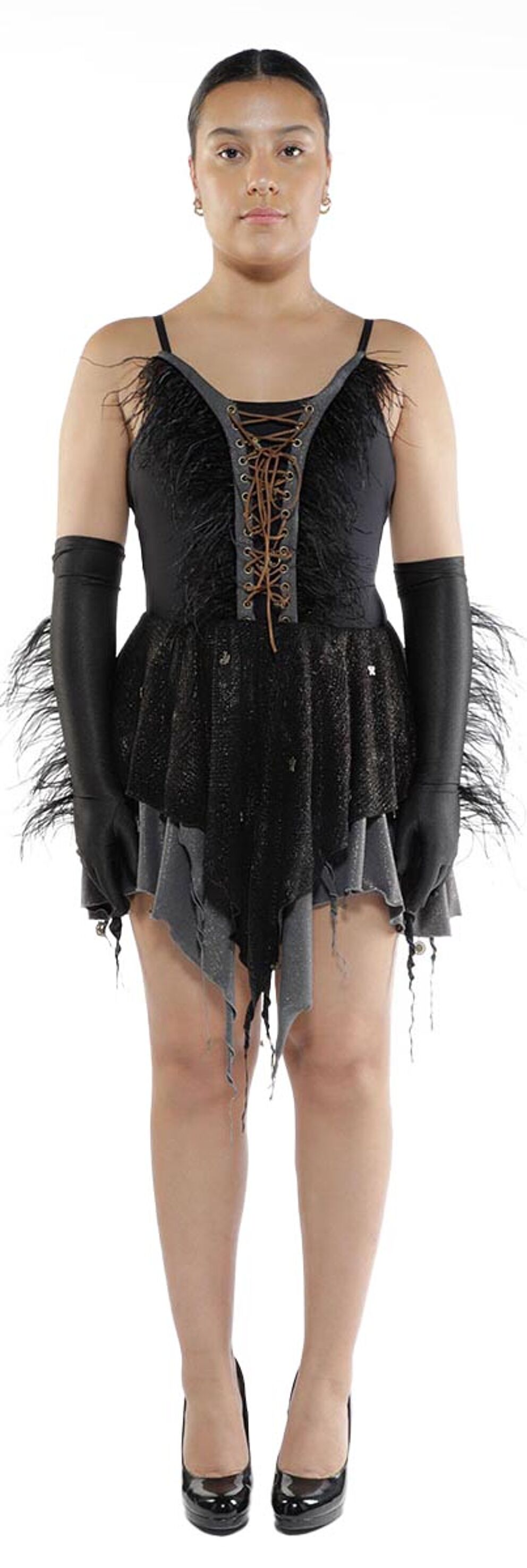 A young woman with tan skin and dark hair stands against a white background wearing a black feathered dress with a lace-up bodice, long black gloves, and black heels.