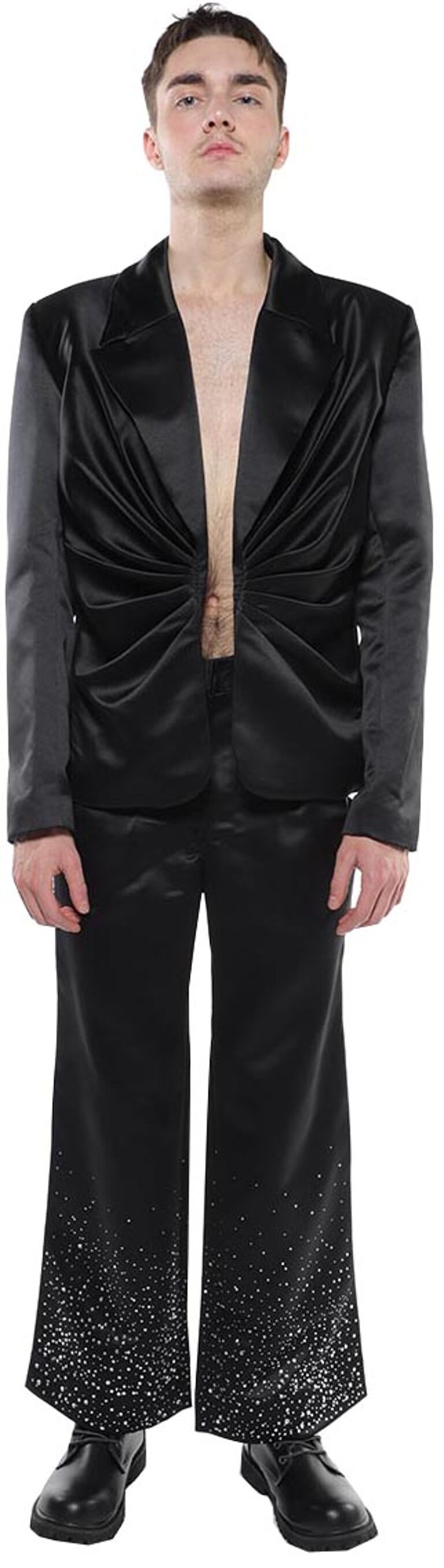 A man in a black satin suit with a pleated top and sparkly bottom stands against a white background.