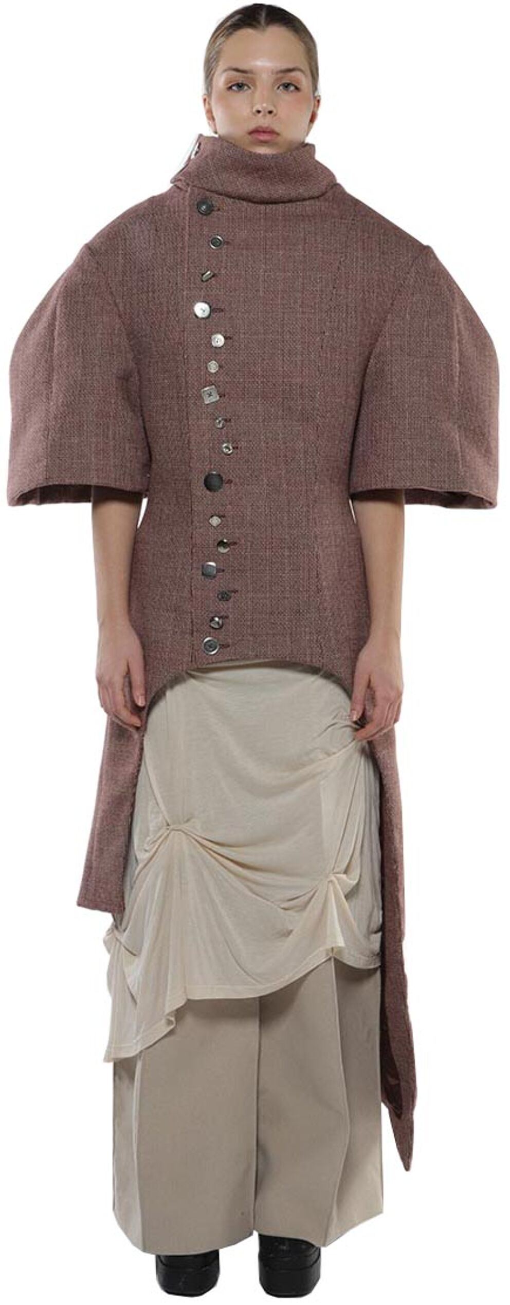 A woman models a mauve, high-low jacket with large sleeves and decorative buttons over a beige, draped skirt and pants.