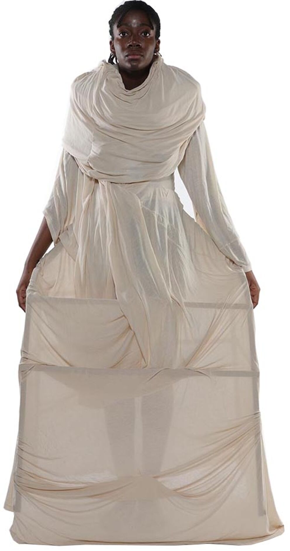 A person with dark skin and short hair wears a long, loose-fitting, beige garment that drapes and folds around them.
