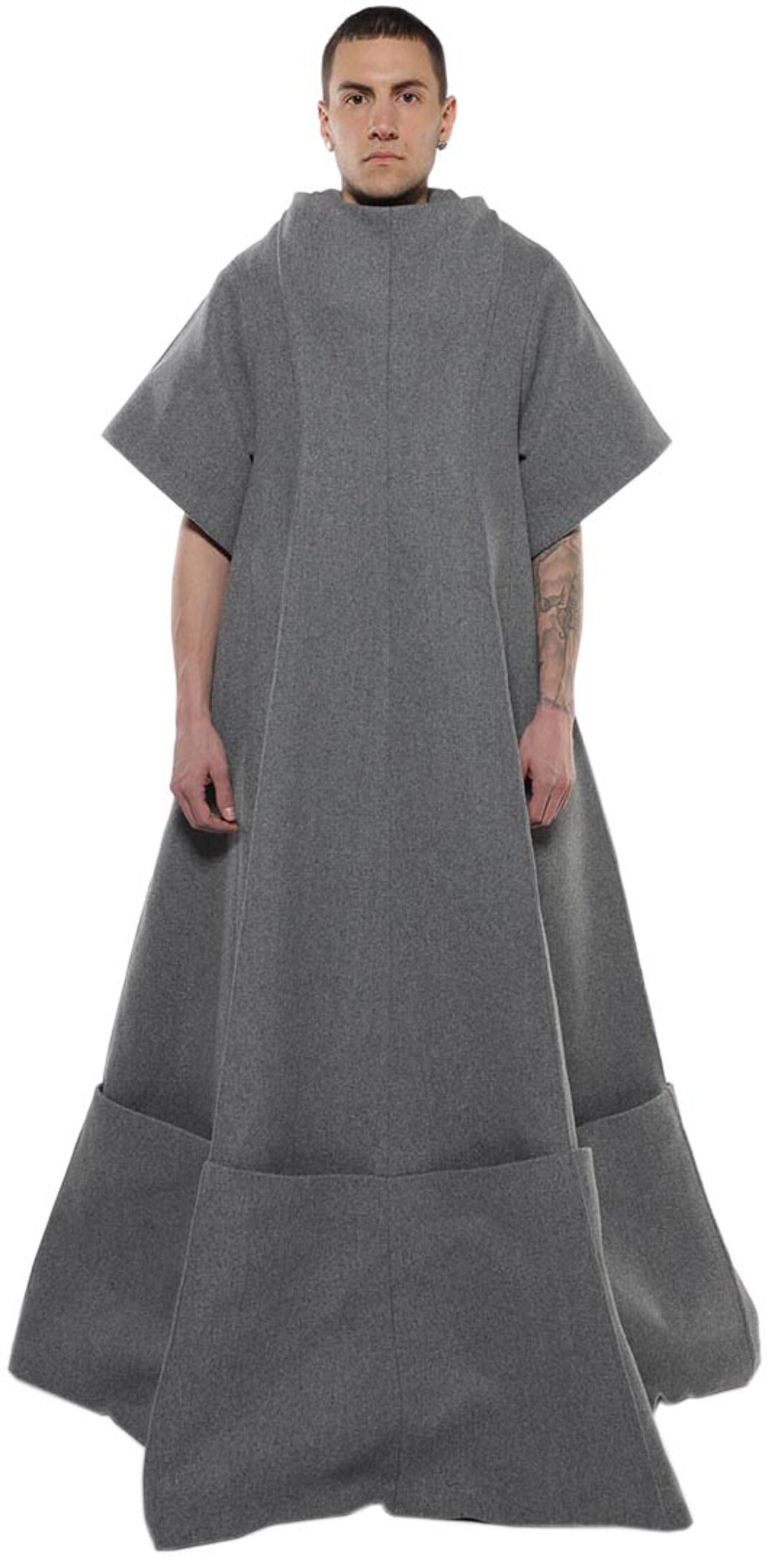 A man with short brown hair models a long, gray, loose-fitting tunic with short sleeves and pockets at the hem.