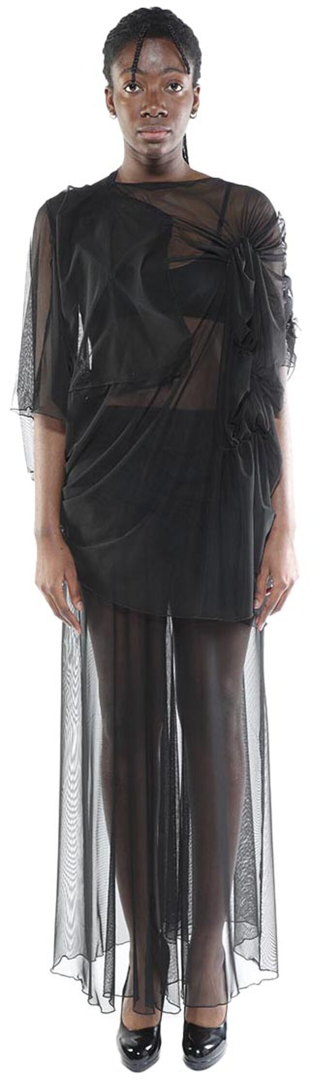 A dark-skinned person with short hair is modeling a sheer black maxi dress with a draped bodice and a fitted underlayer.