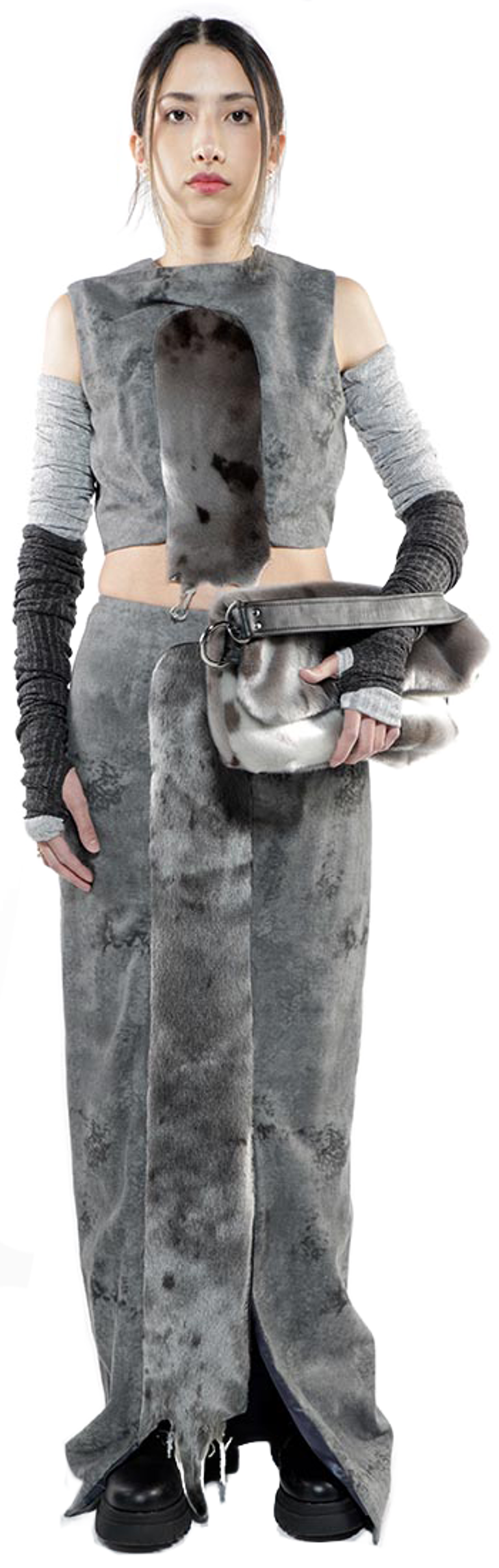 A young woman with dark hair pulled back in a bun models a gray faux fur outfit consisting of a sleeveless crop top, long sleeves, and a floor-length skirt, carrying a matching faux fur handbag.