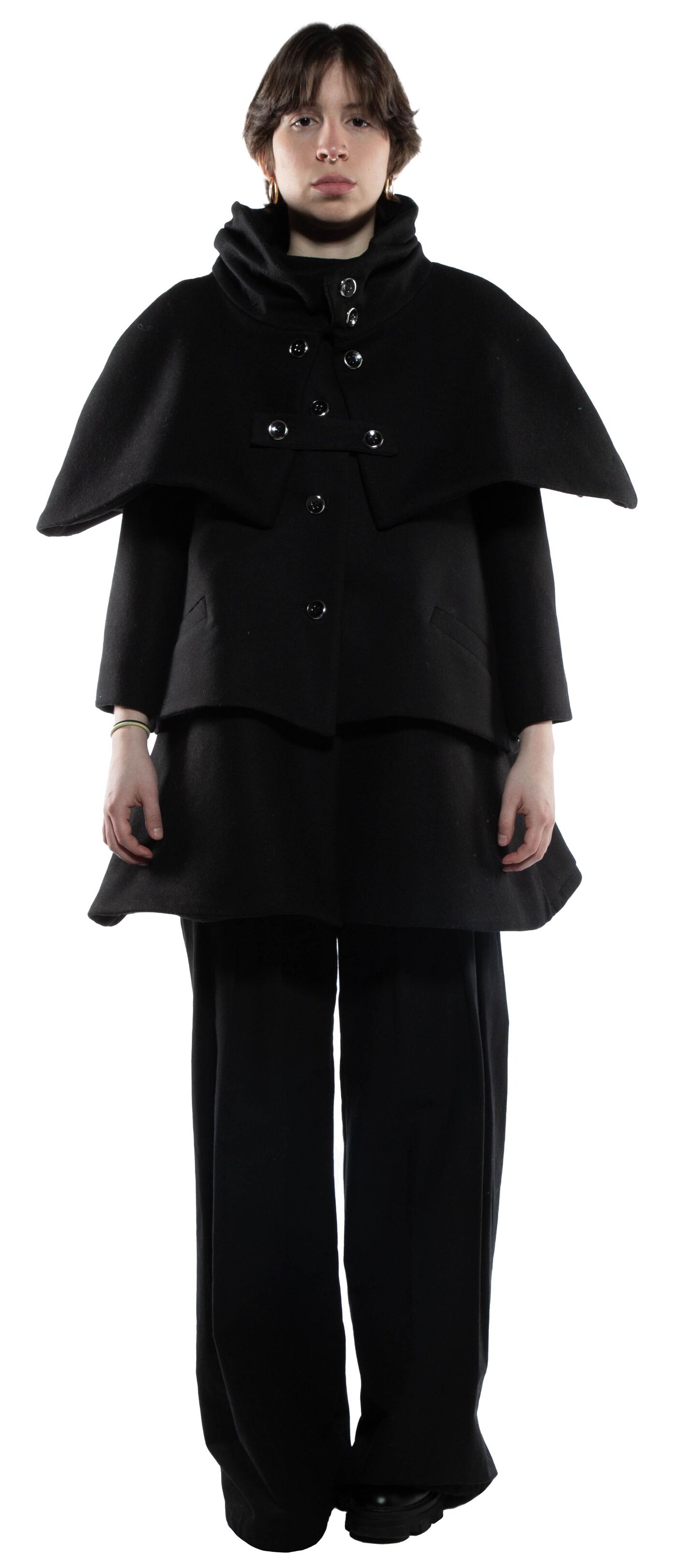 A person wearing a black coat with a cape and black trousers stands against a white background.