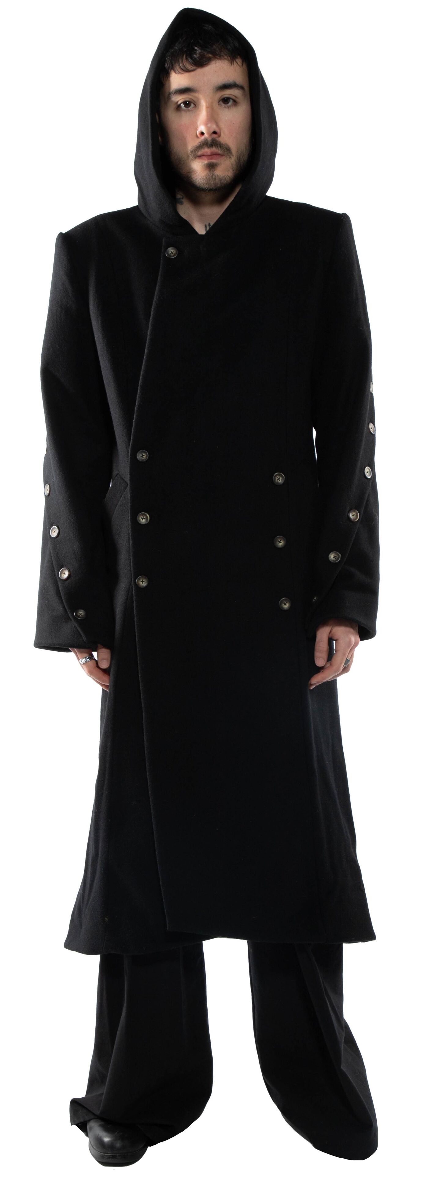A person wearing a black hooded coat with silver buttons stands against a white background.