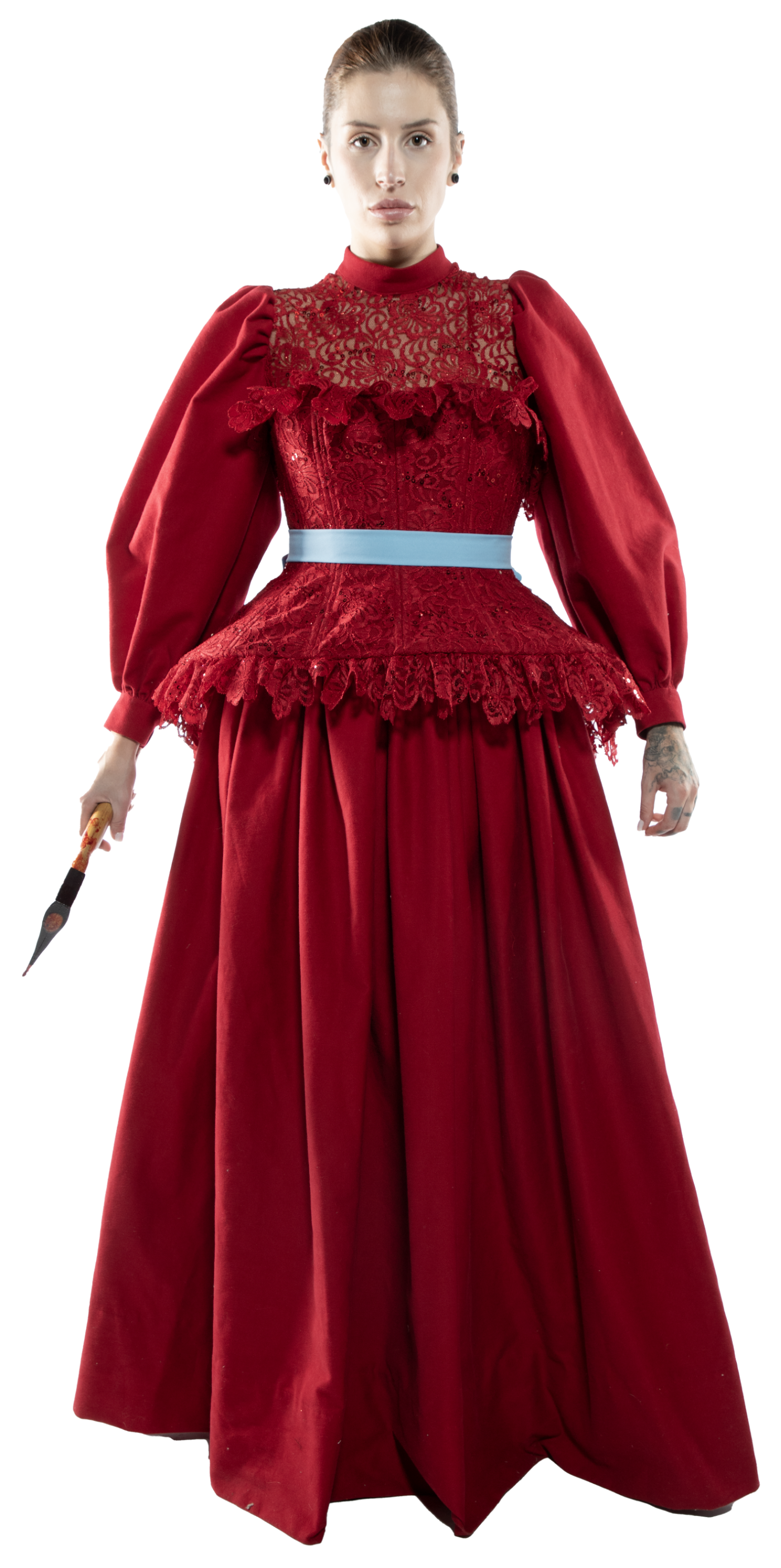 A woman in a long, red, lace-trimmed gown with puffy sleeves and a light blue belt holds a dark object resembling a paintbrush or knife in her left hand.
