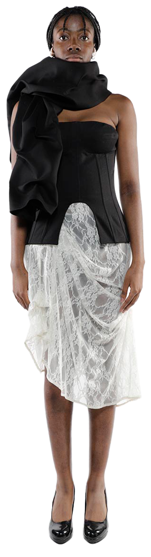 A dark-skinned model with short black hair wears a black corset-style top with a large black fabric draped over one shoulder, a draped off-white lace skirt, and black heels.