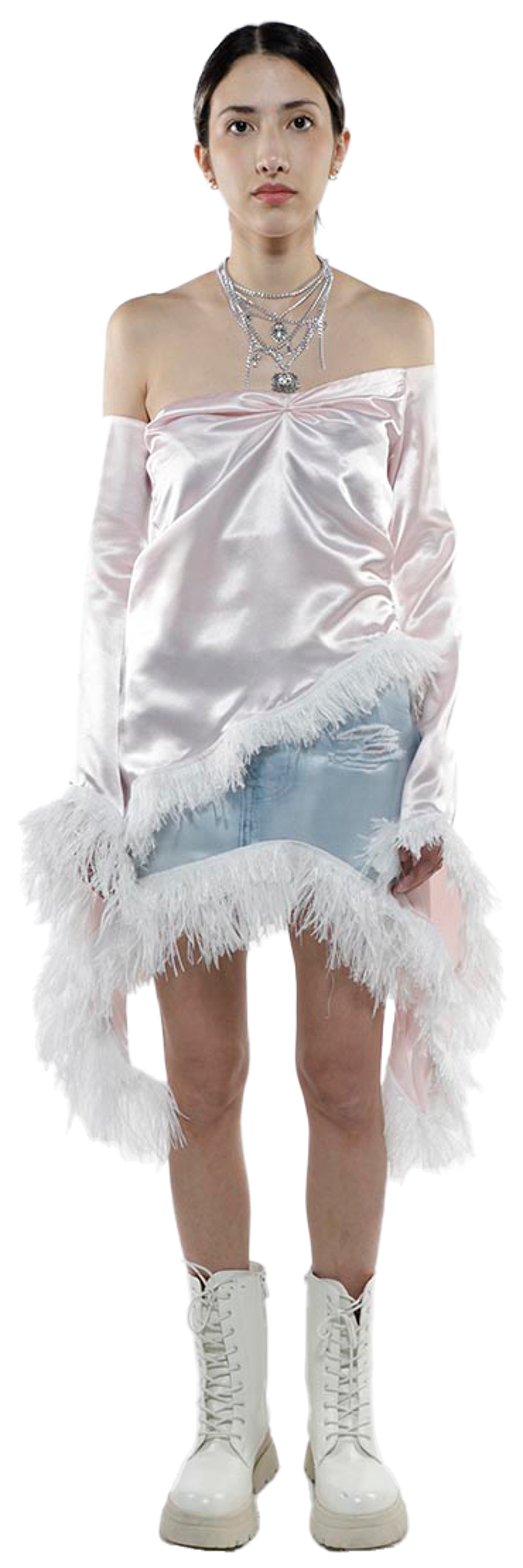 A young woman with dark hair and fair skin models a pink satin off-the-shoulder top with long sleeves and white feather trim, paired with a light blue denim mini-skirt and white combat boots.