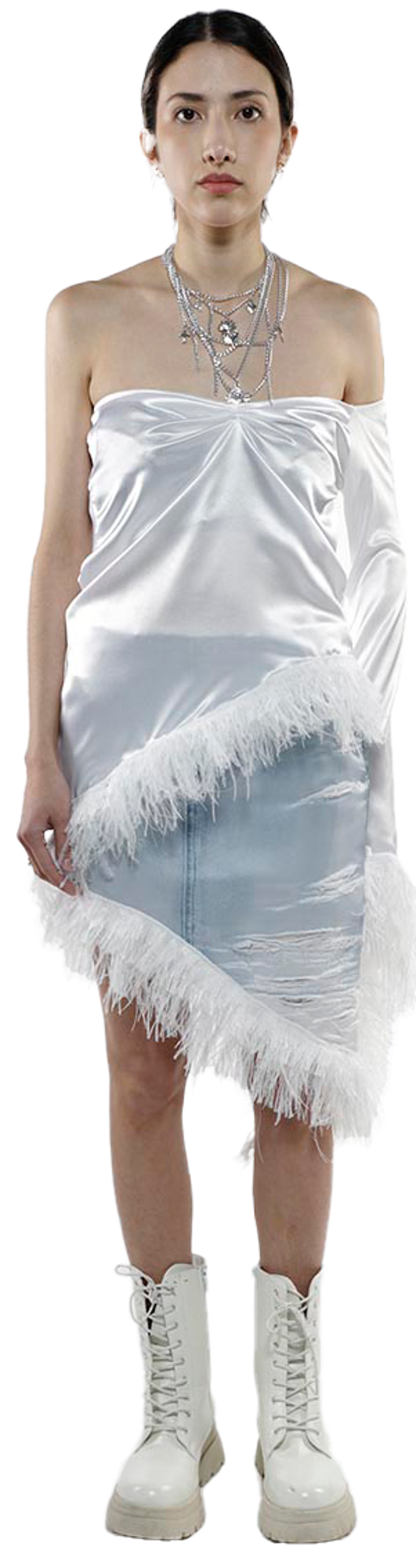 A young woman with dark hair and a neutral expression models a white satin one-shoulder top with a feathered hemline, paired with a light blue denim mini skirt, and white lace-up boots.