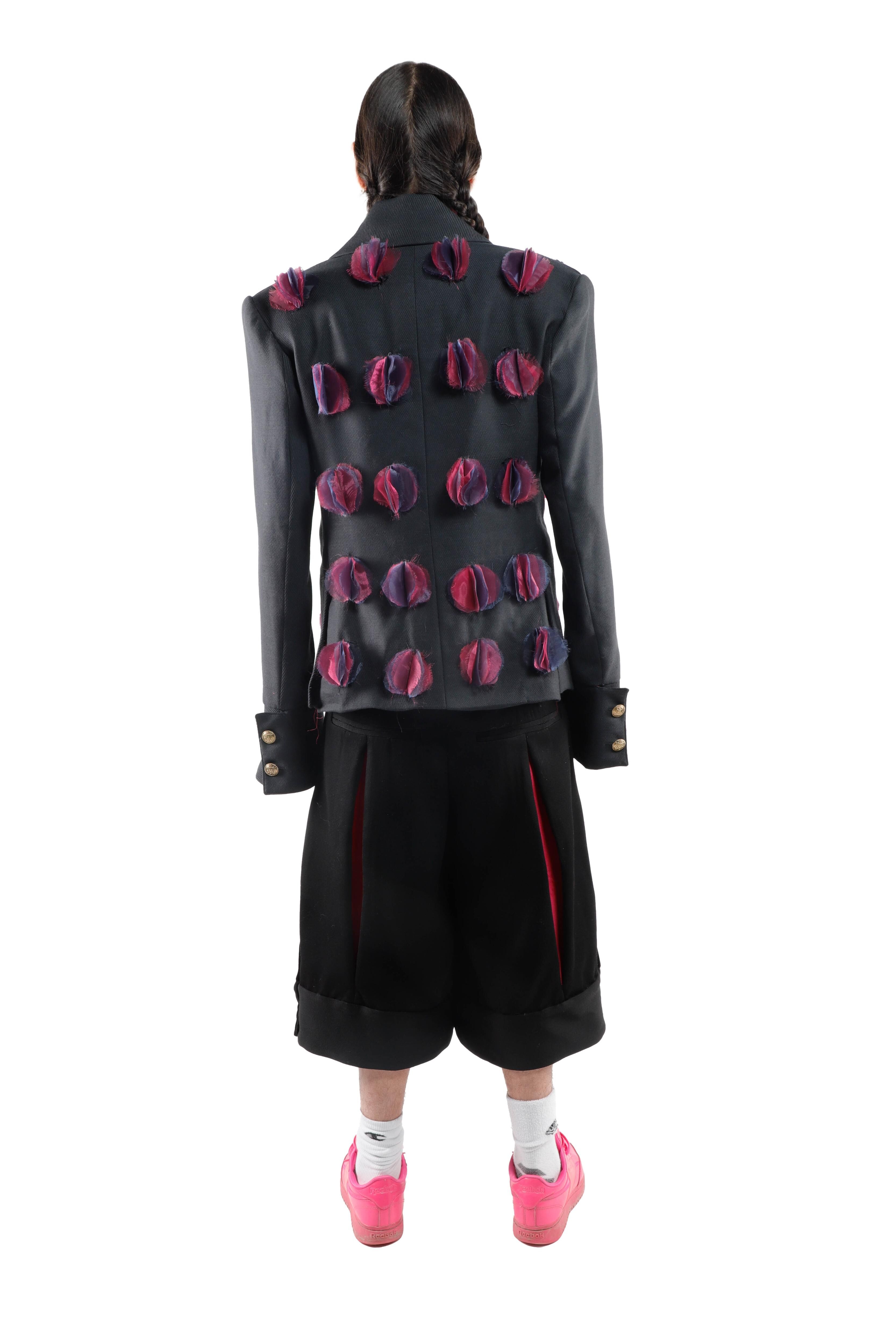 This image features a dark gray jacket adorned with red and purple floral details, paired with black shorts and bright pink sneakers.