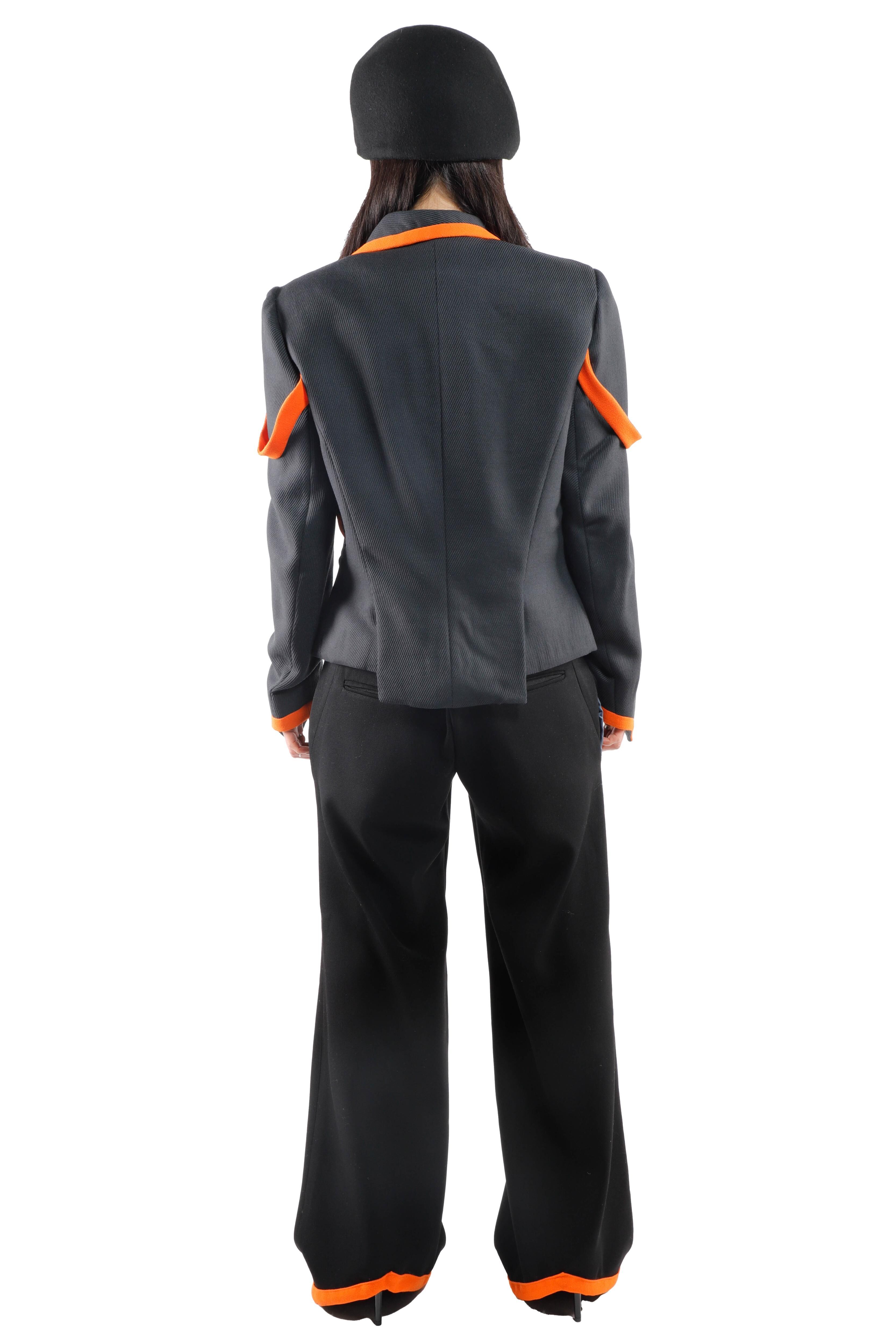 This image shows the back of a person wearing a gray jacket with orange accents and wide black pants, completing the look with a black hat.