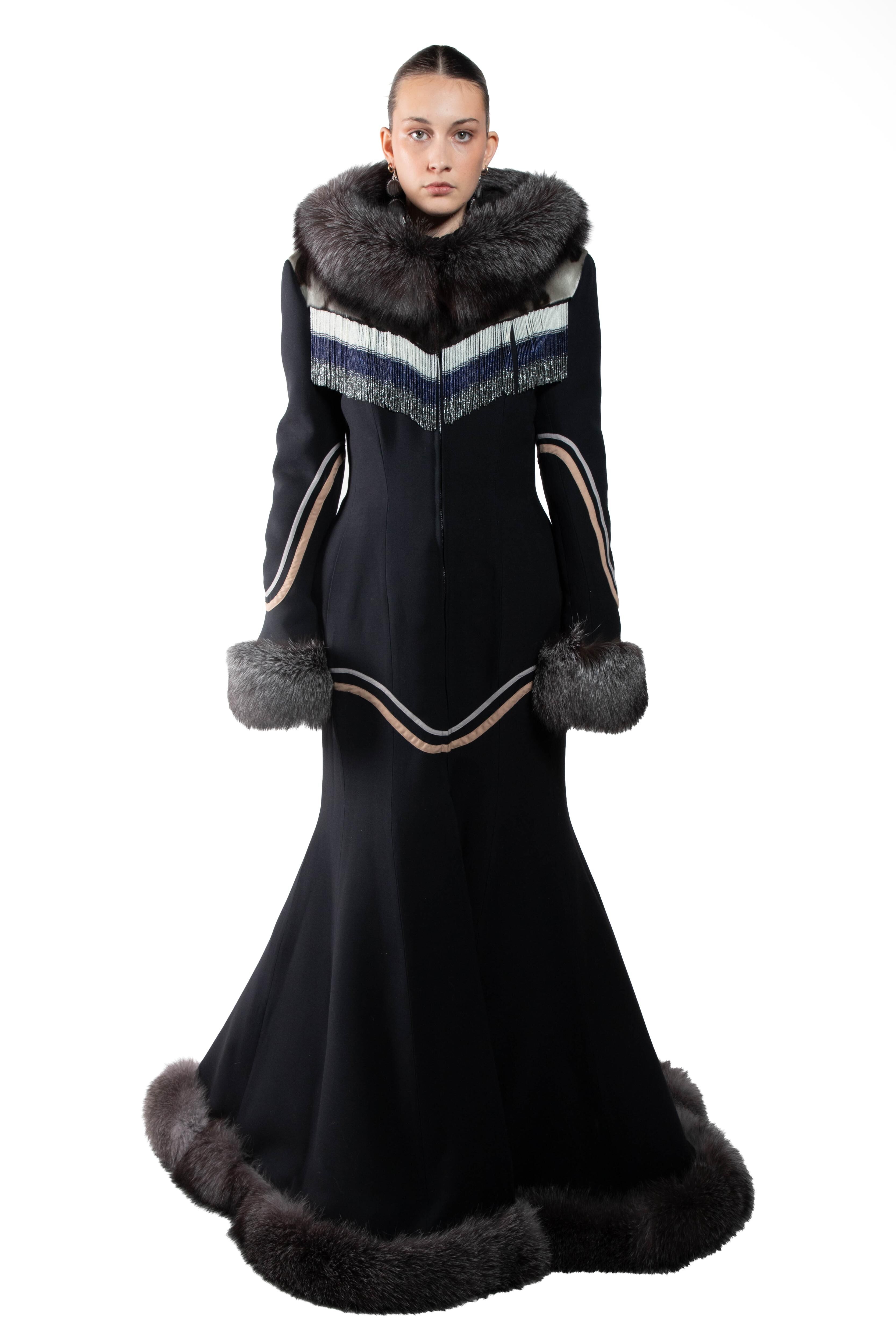 A striking black gown with fur accents on the collar, cuffs, and hem, featuring intricate ethnic-inspired detailing on the bodice and sleeves, creating an elegant, form-fitting silhouette that flares at the bottom.