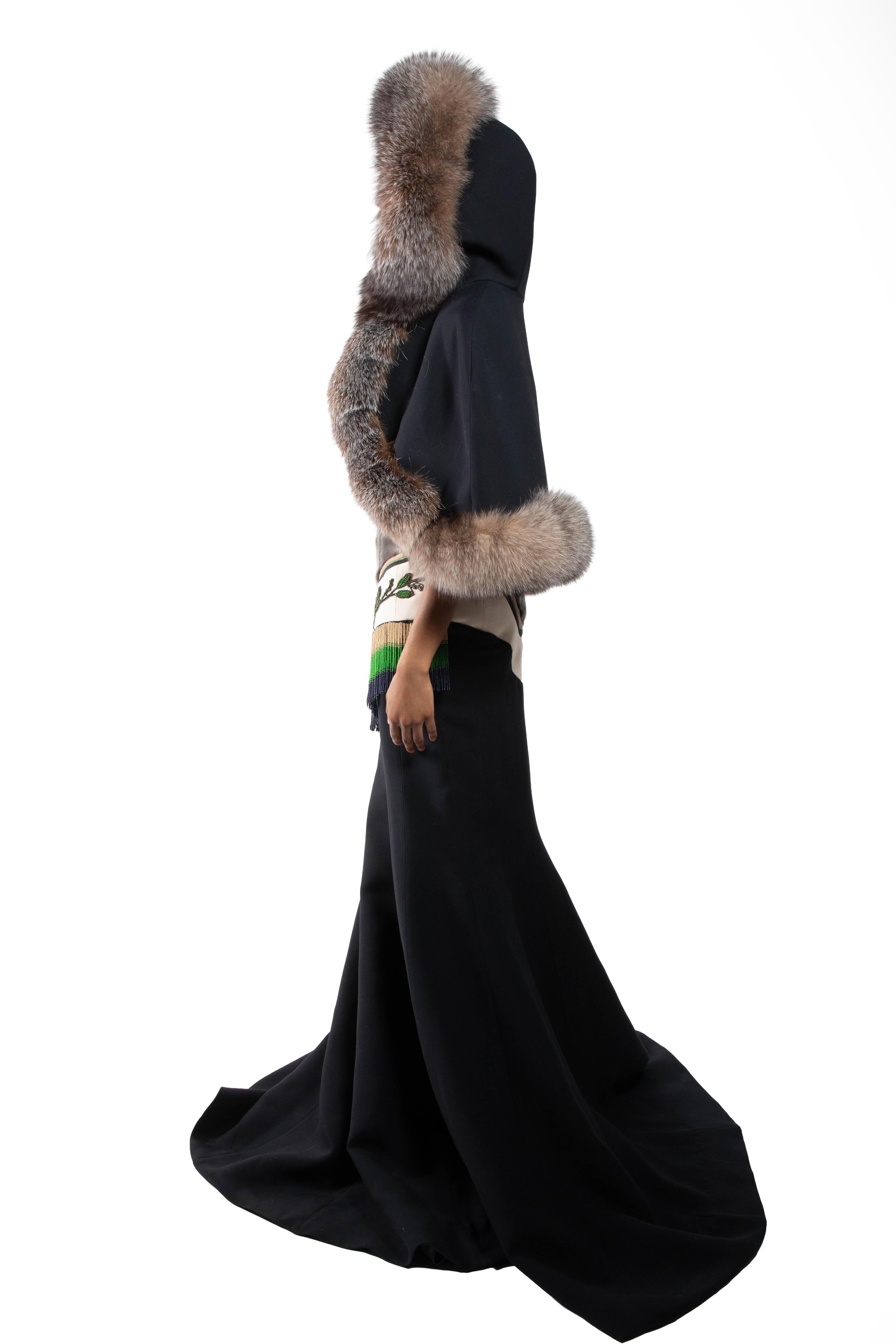 A woman in a long black dress and a hooded cape adorned with animal fur, showing a glimpse of her undergarments.