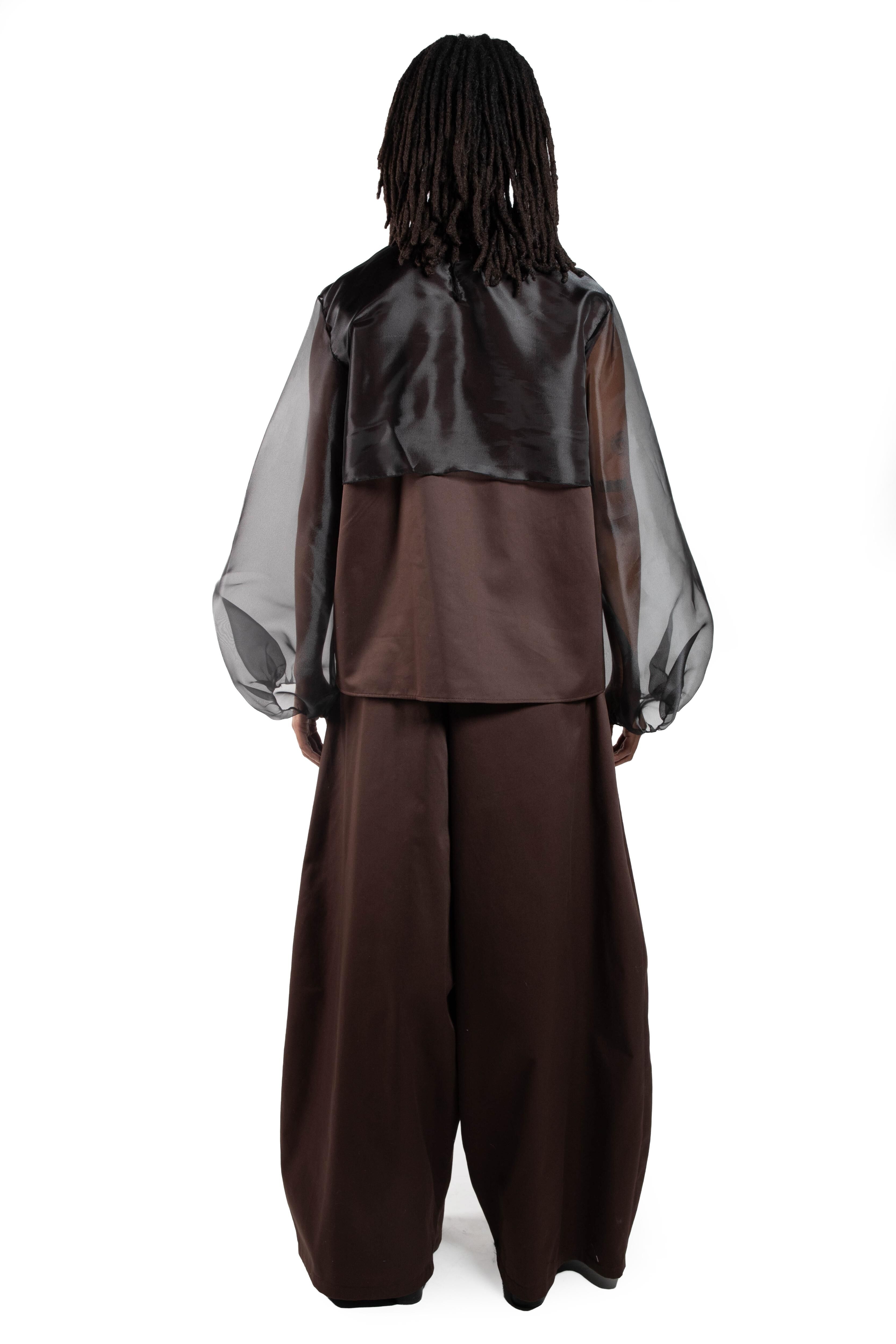 This image shows a person from behind, wearing a brown silk blouse with sheer black organza sleeves and wide brown pants.