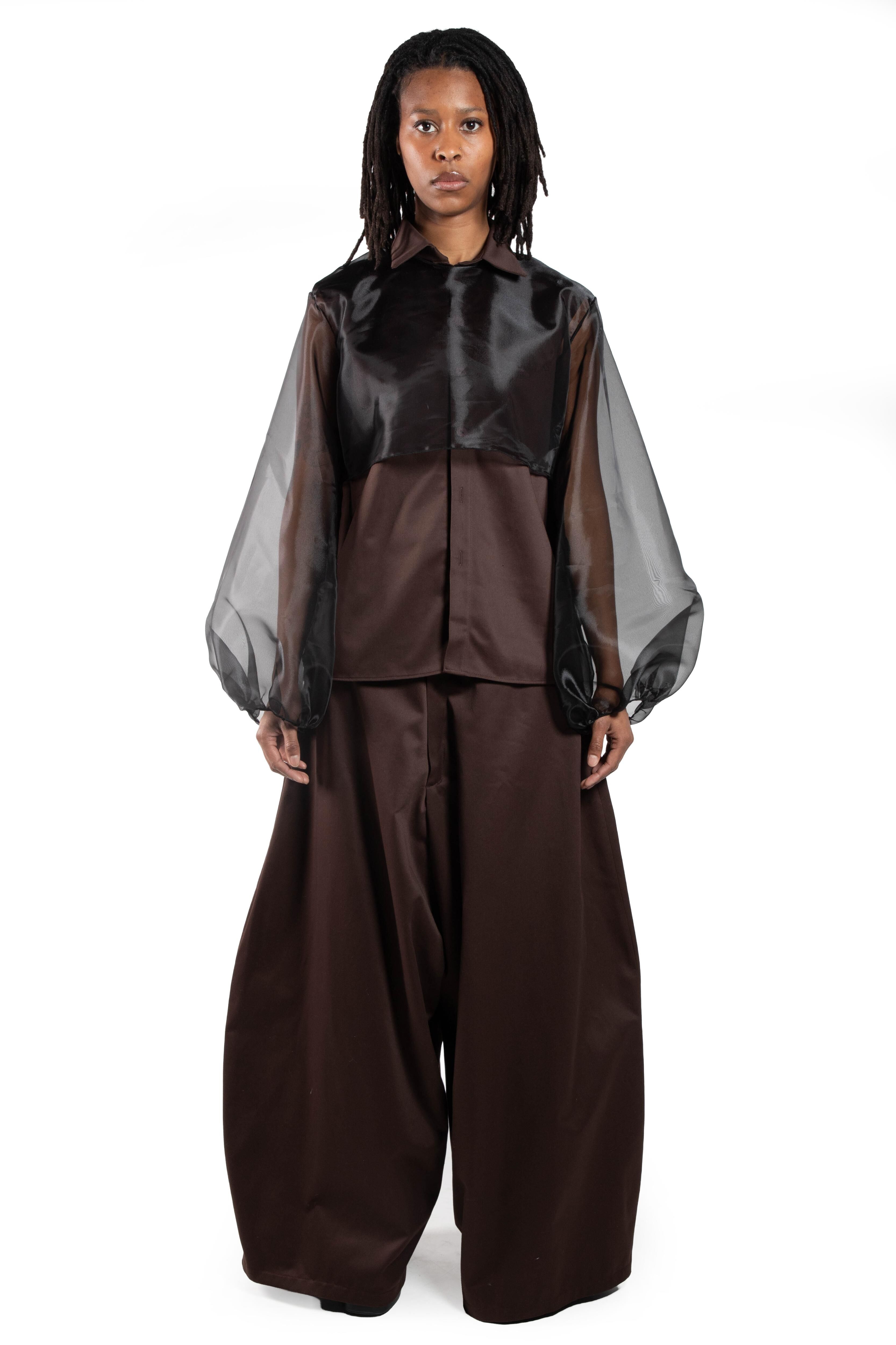 This model wears a brown silk long-sleeved blouse with sheer black organza panels on the shoulders and sleeves, paired with wide brown trousers.