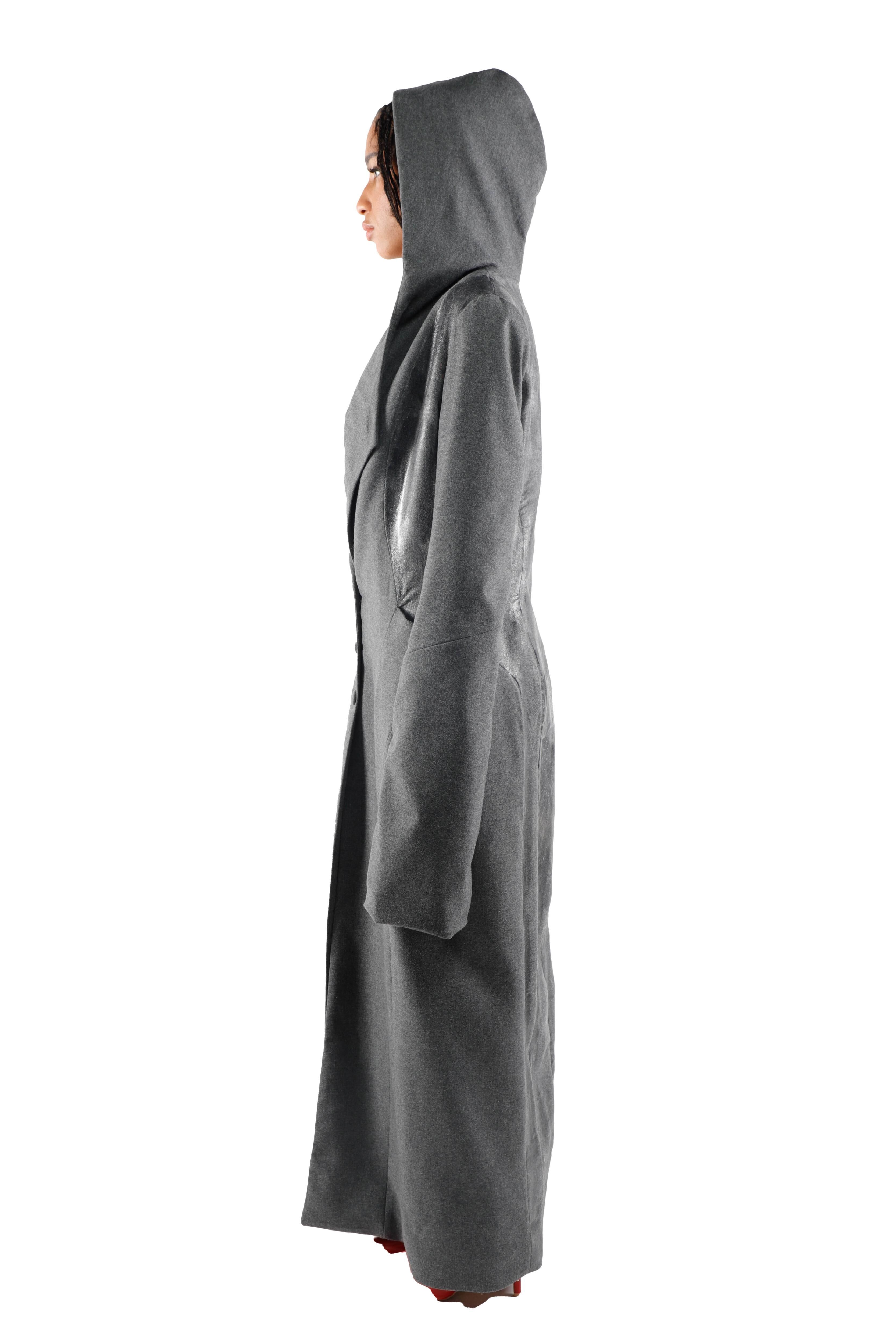 This is an image of a woman in profile wearing a long, dark, hooded coat. The background is white, making the clothing stand out.