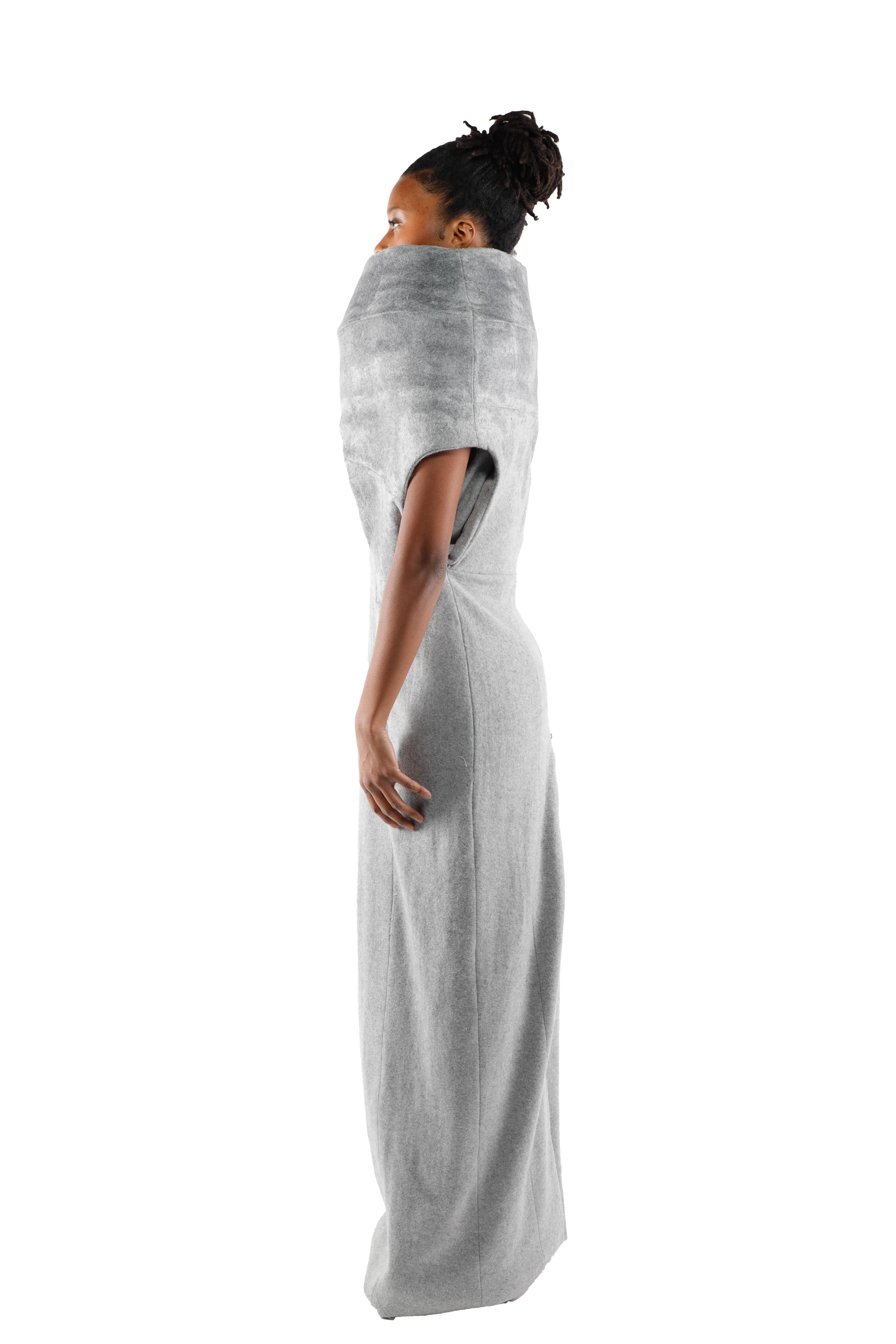 This image features a woman in profile, wearing a light gray, form-fitting, floor-length dress. The dress has a voluminous and abstract neckline design, resembling a scarf or collar.