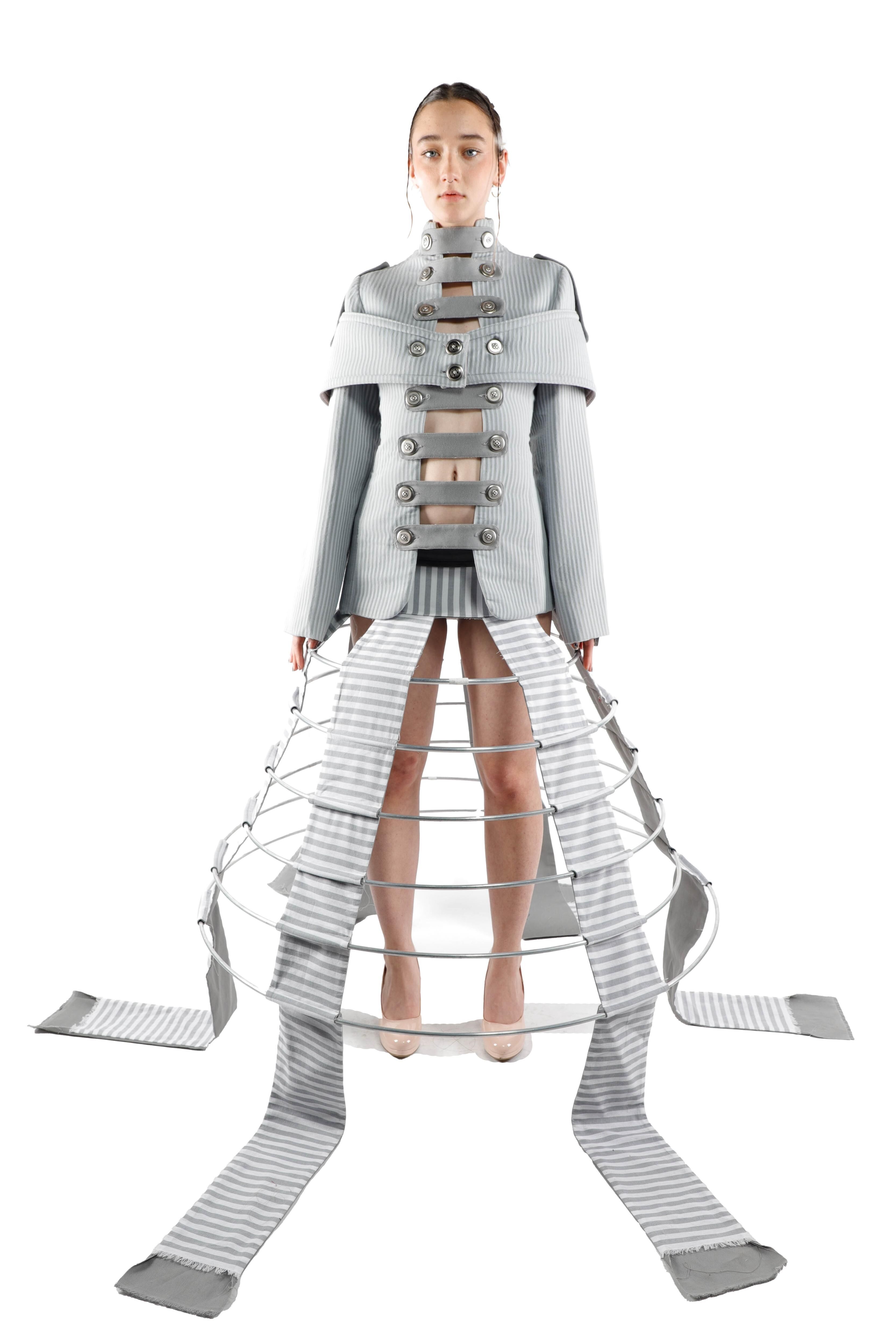 This image features a woman wearing a conceptual gray outfit with a cage-like structure and long sashes. The design is avant-garde and striking.