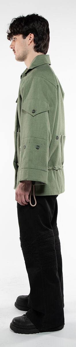 A young man with dark hair, wearing a green jacket, black pants, and black shoes. The image shows him in profile against a white background.