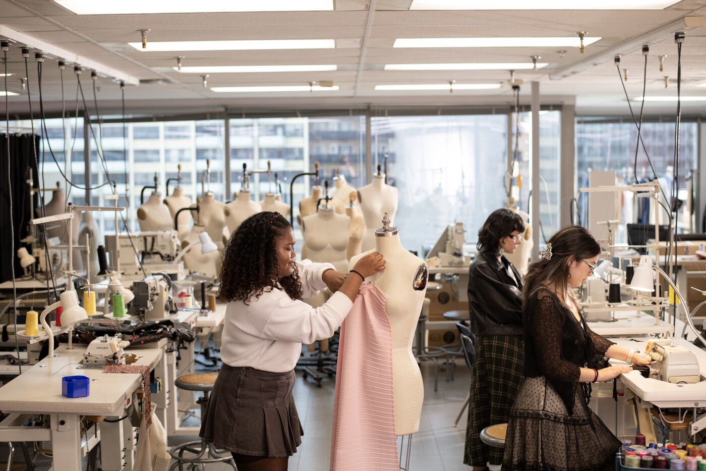 Two women engage in garment creation in a well-equipped fashion design studio, surrounded by mannequins and sewing machines.