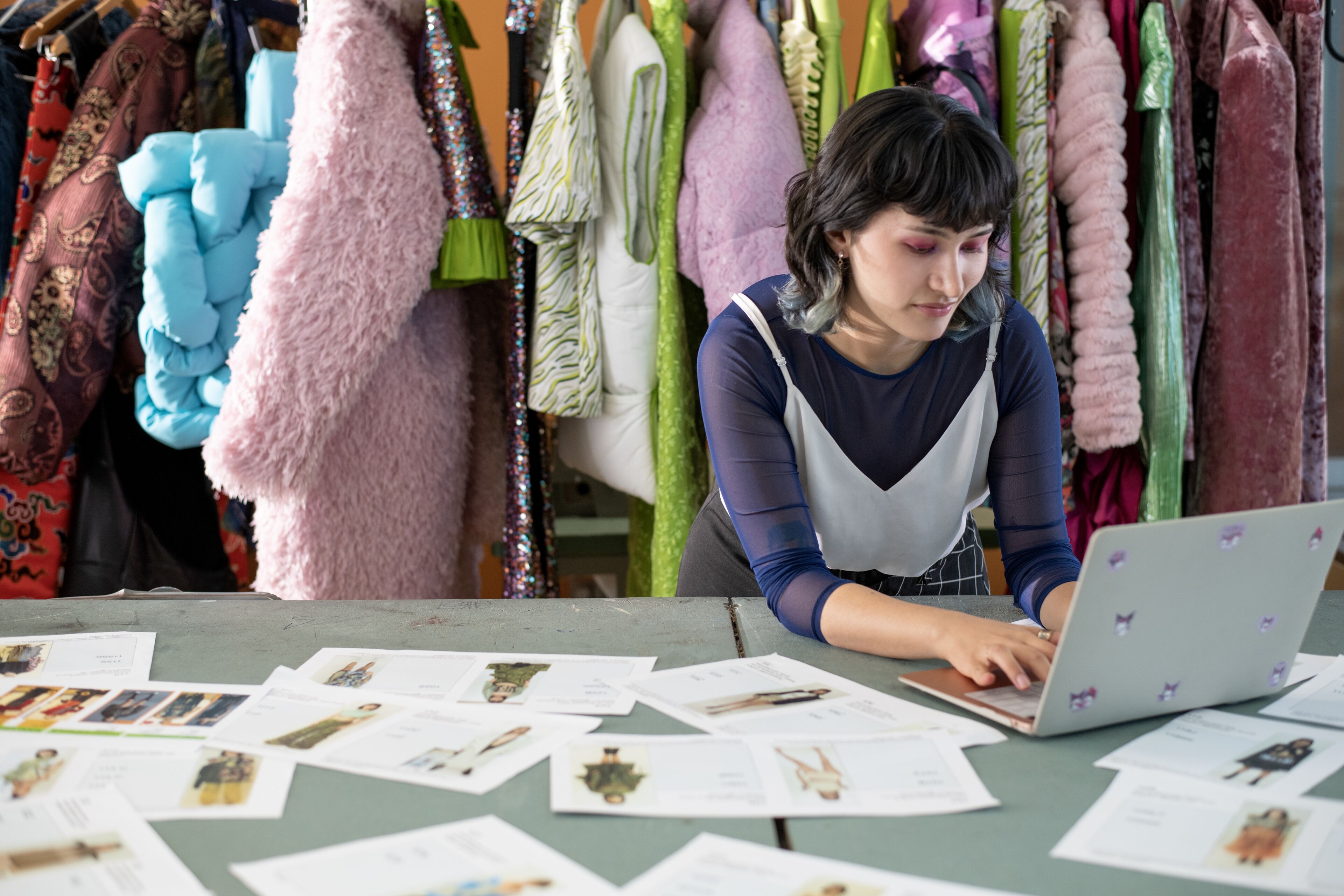 Une créatrice de mode concentrée examine des photos de vêtements parmi des tissus colorés.