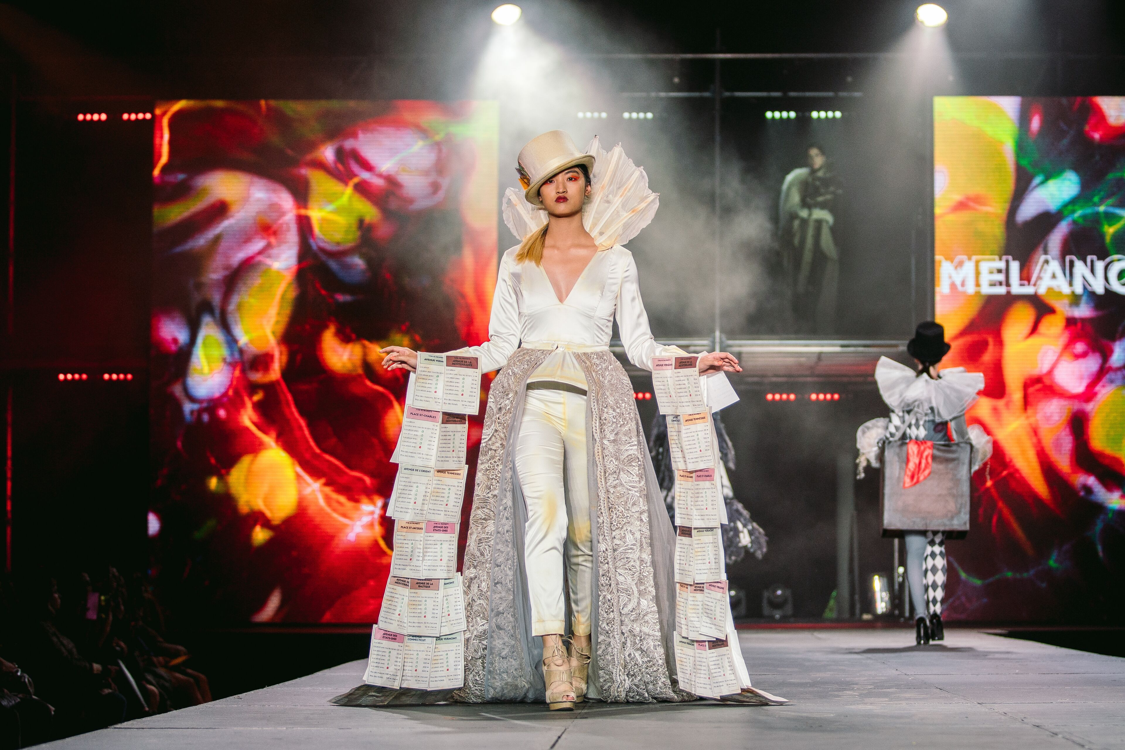 Un mannequin présente avec confiance une tenue créative avec des éléments de journal sur un podium vibrant, incarnant un design novateur.