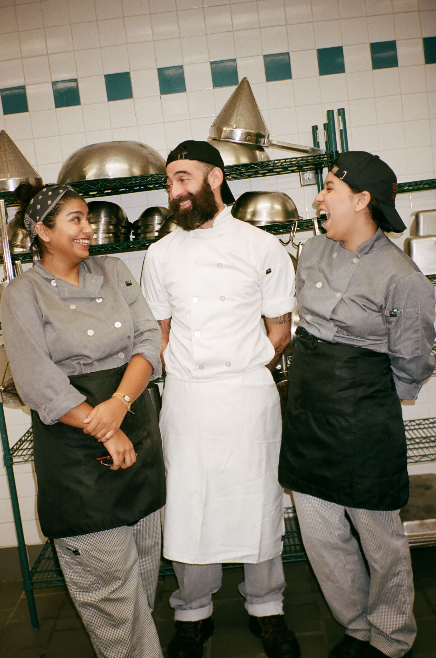 Three chefs in uniform share a light-hearted moment in a commercial kitchen, showcasing camaraderie and a positive work environment.