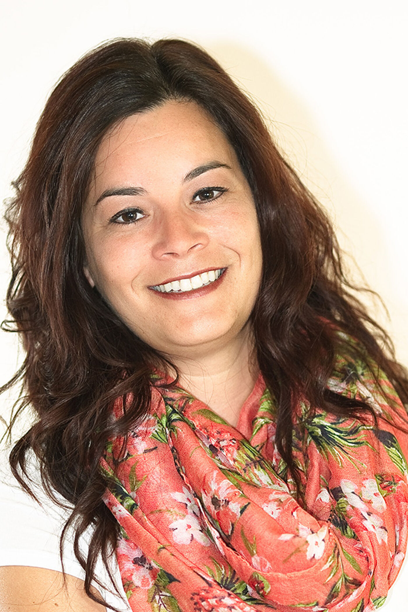 A cheerful woman with shoulder-length brown hair, wearing a vibrant floral scarf.