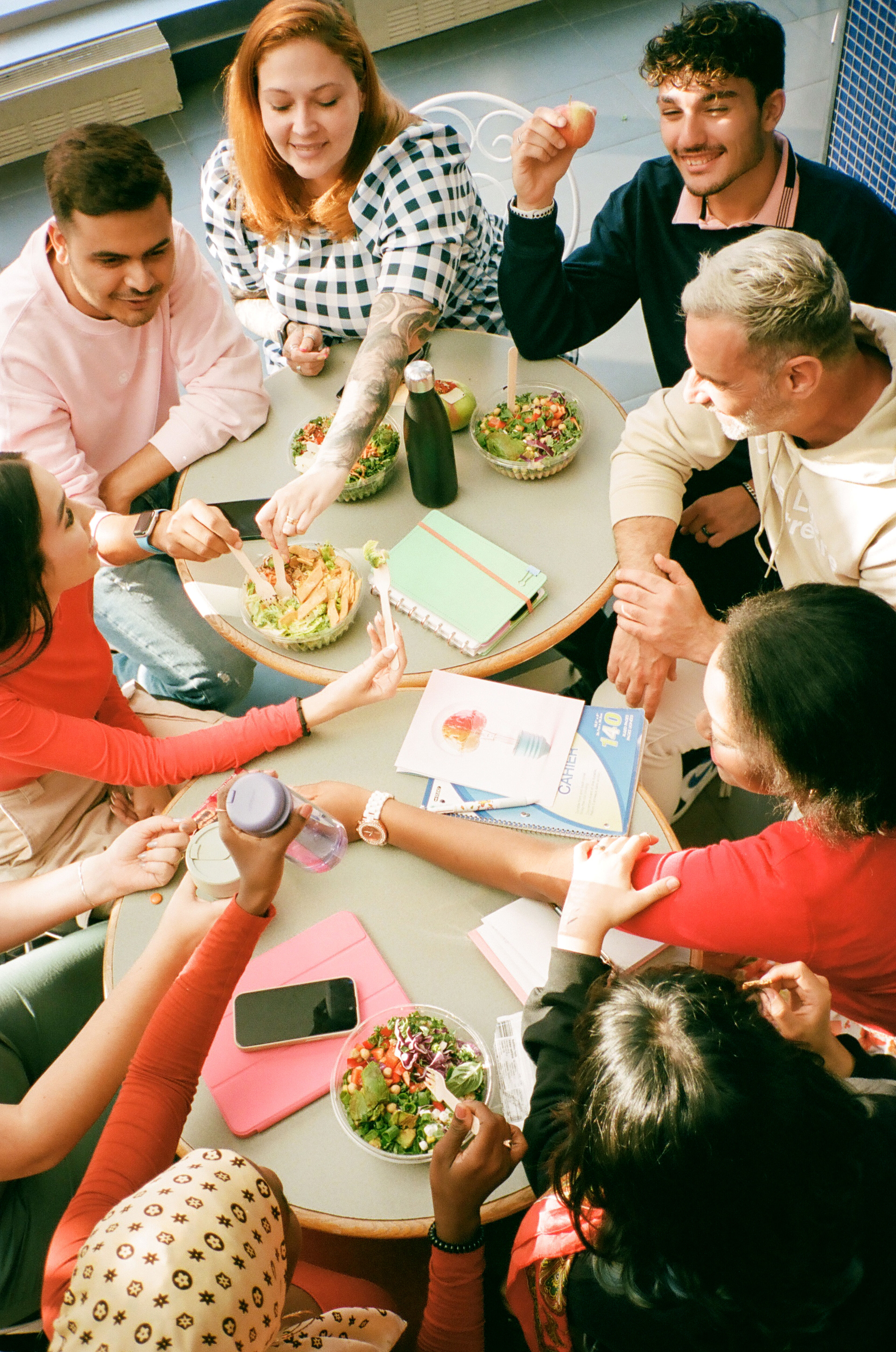 Un groupe hétérogène de personnes de différents âges discute autour d'une table garnie de salades saines, de livres et de smartphones.