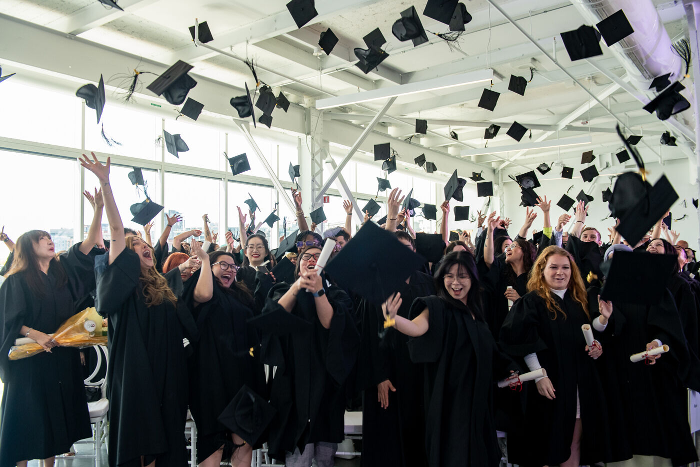 A joyful group of graduates throwing their caps in the air in a ceremony hall.