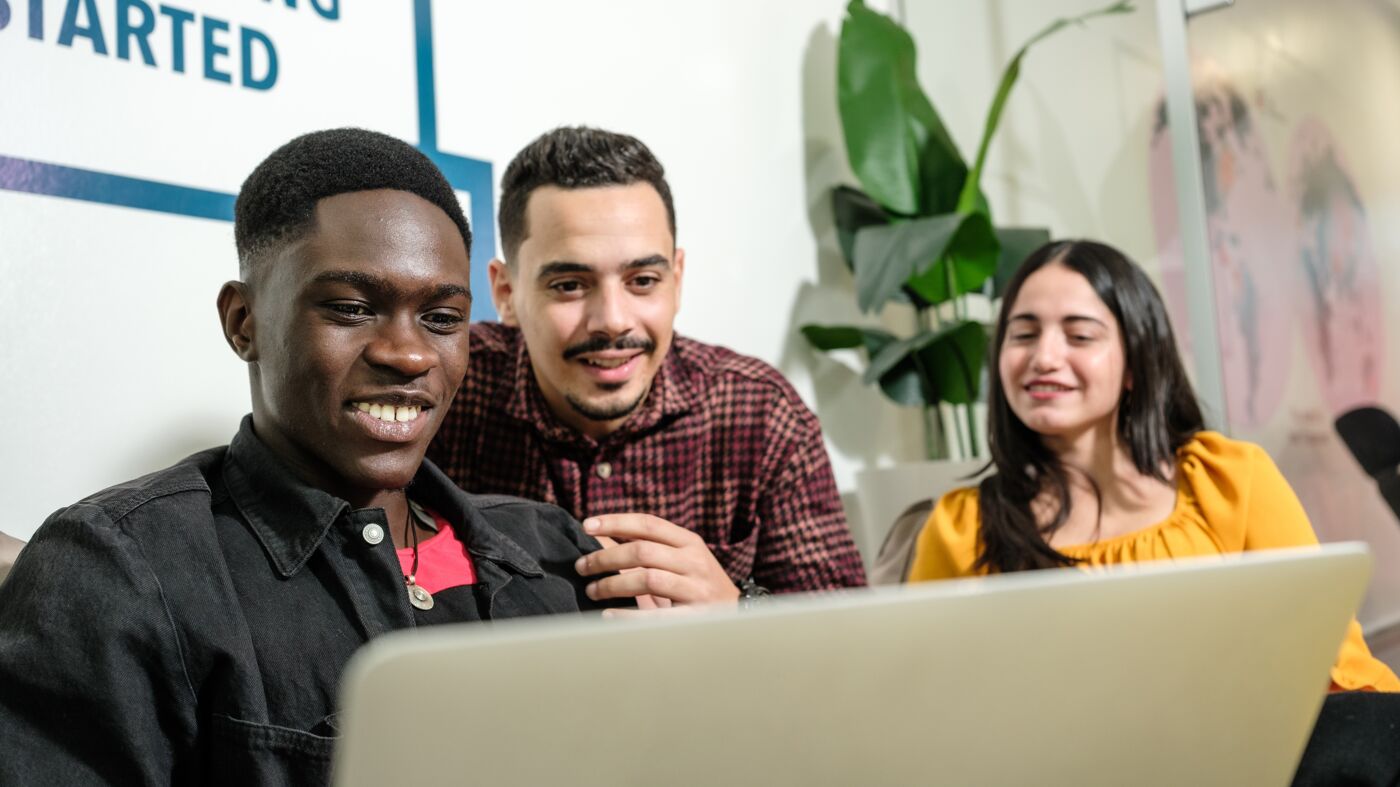 Three students with a laptop sharing a joyful learning moment.