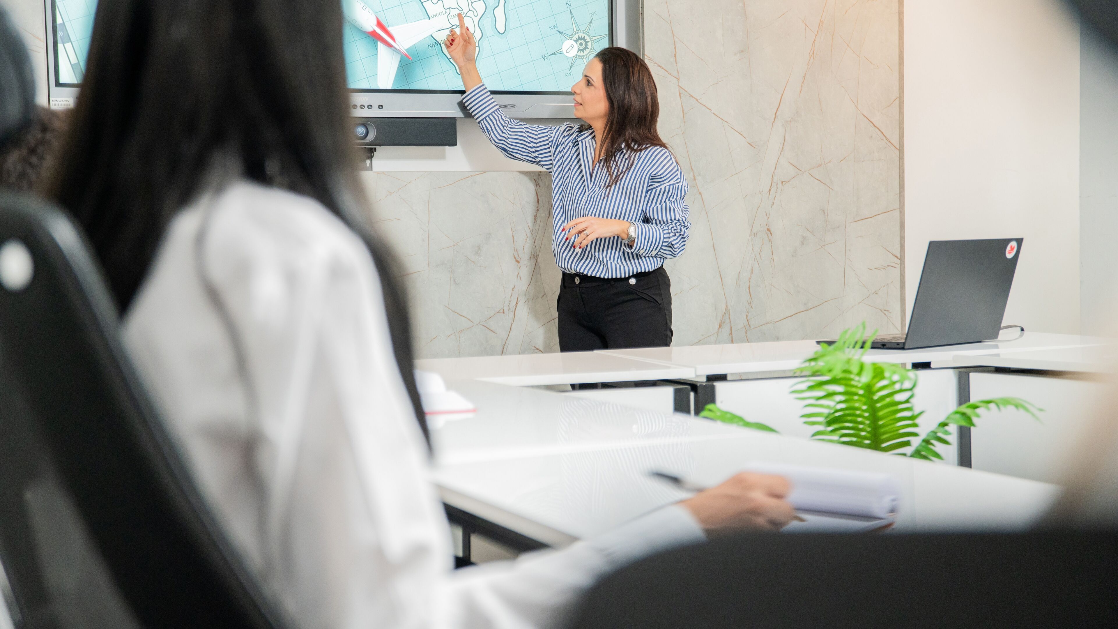 A professional woman delivers a presentation in a modern office, engaging with her audience.