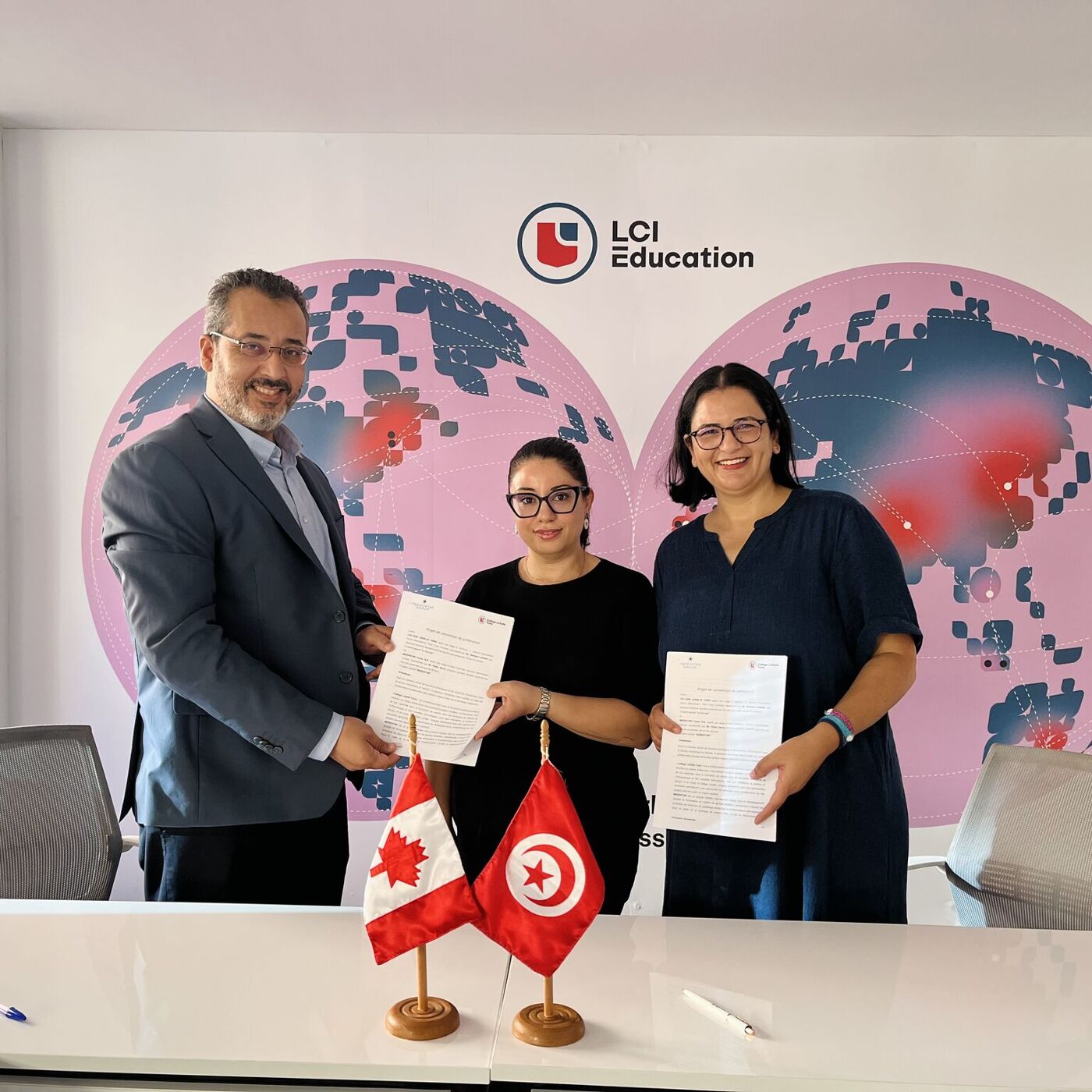 Three people are standing behind a table with flags, holding documents, likely after signing an agreement. The backdrop features a globe and the LCI Education logo, suggesting an international educational partnership.