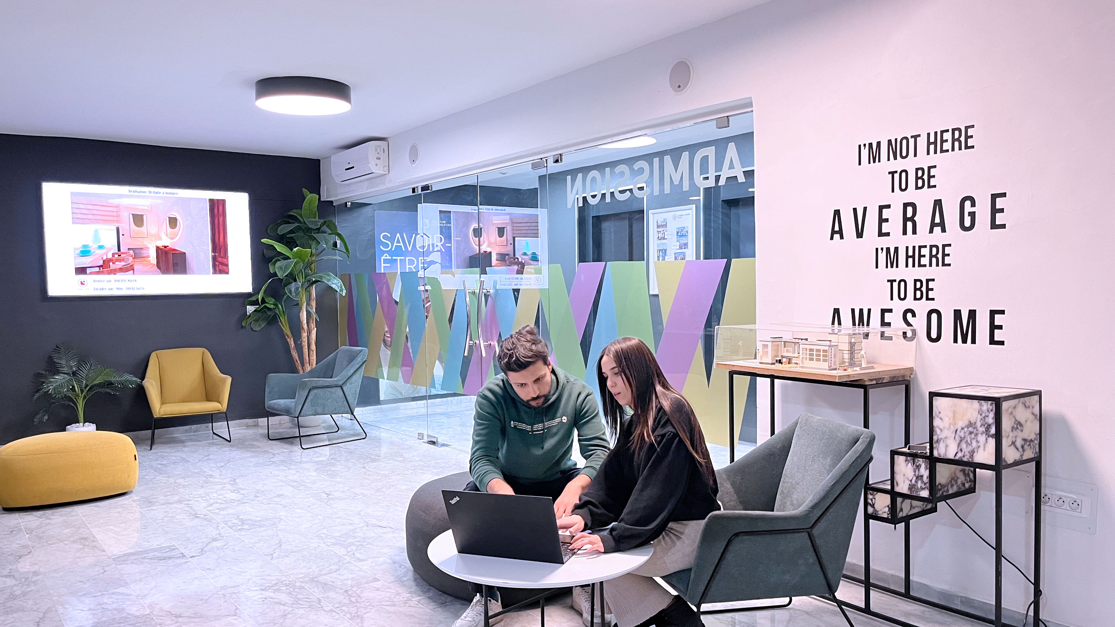 Two professionals collaborating on a laptop in a vibrant, modern office lounge, with motivational decor.