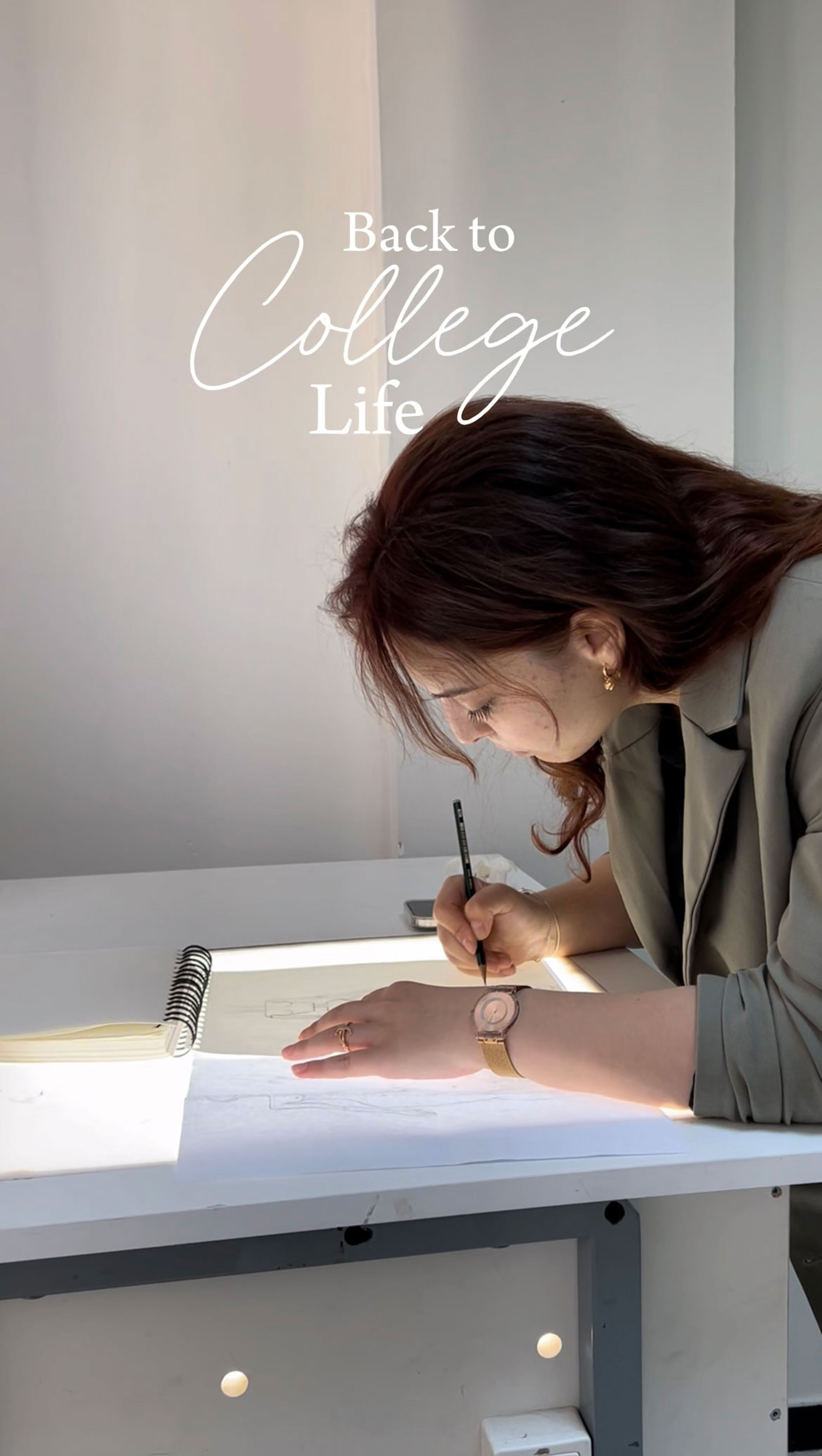  A student leans over a light table, focused on sketching in her notebook. The phrase "Back to College Life" overlays the image, capturing the return to academic routines and creative studies.