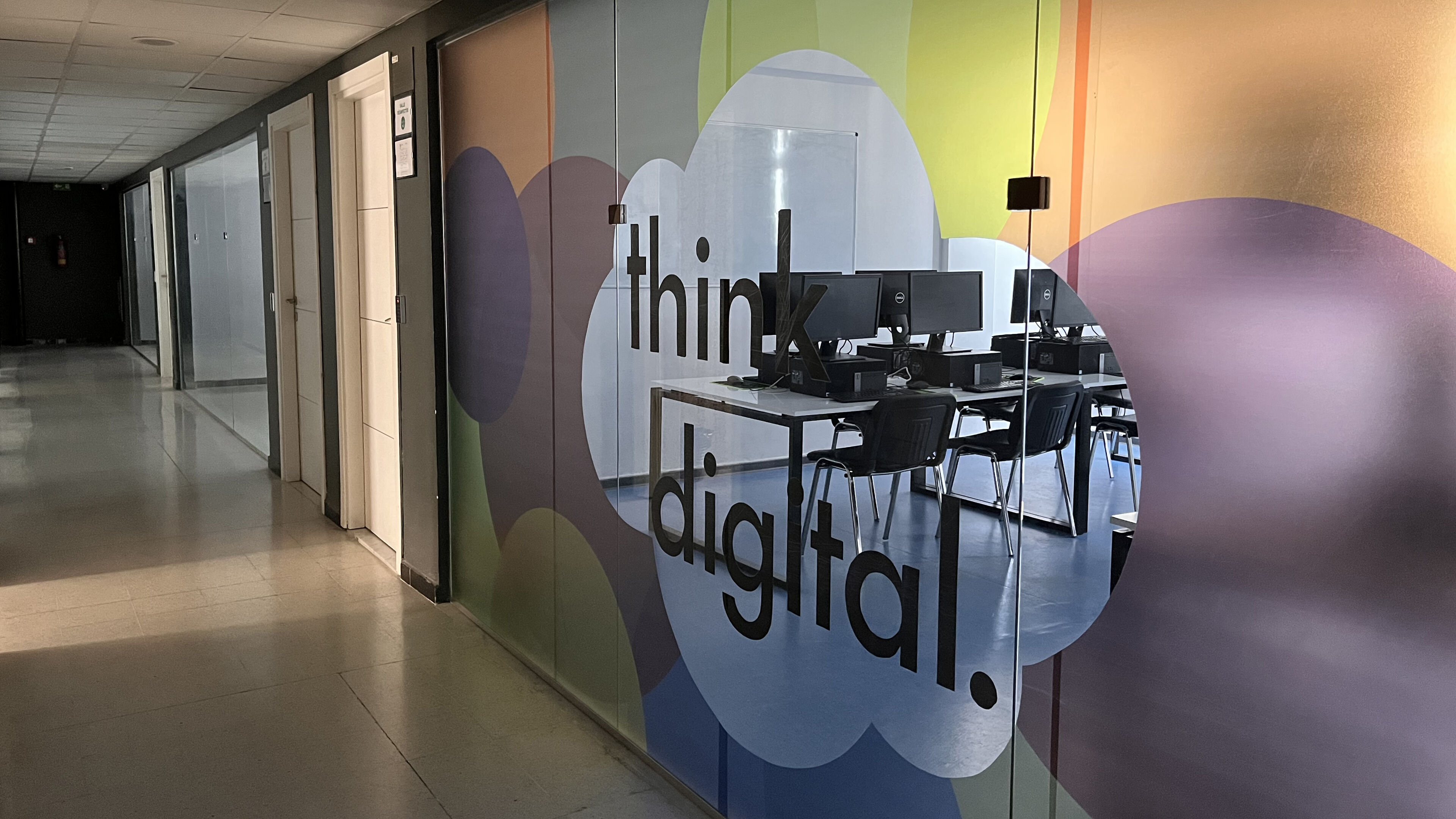 A sleek corridor in a corporate setting featuring a semi-transparent partition with the phrase "think digital." Modern desks and computers are visible through the glass, showcasing a contemporary workspace.