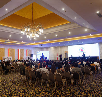 Vue des participants assis dans une grande salle, concentrés sur un intervenant lors d'une conférence d'affaires, avec d'élégants lustres au-dessus.
