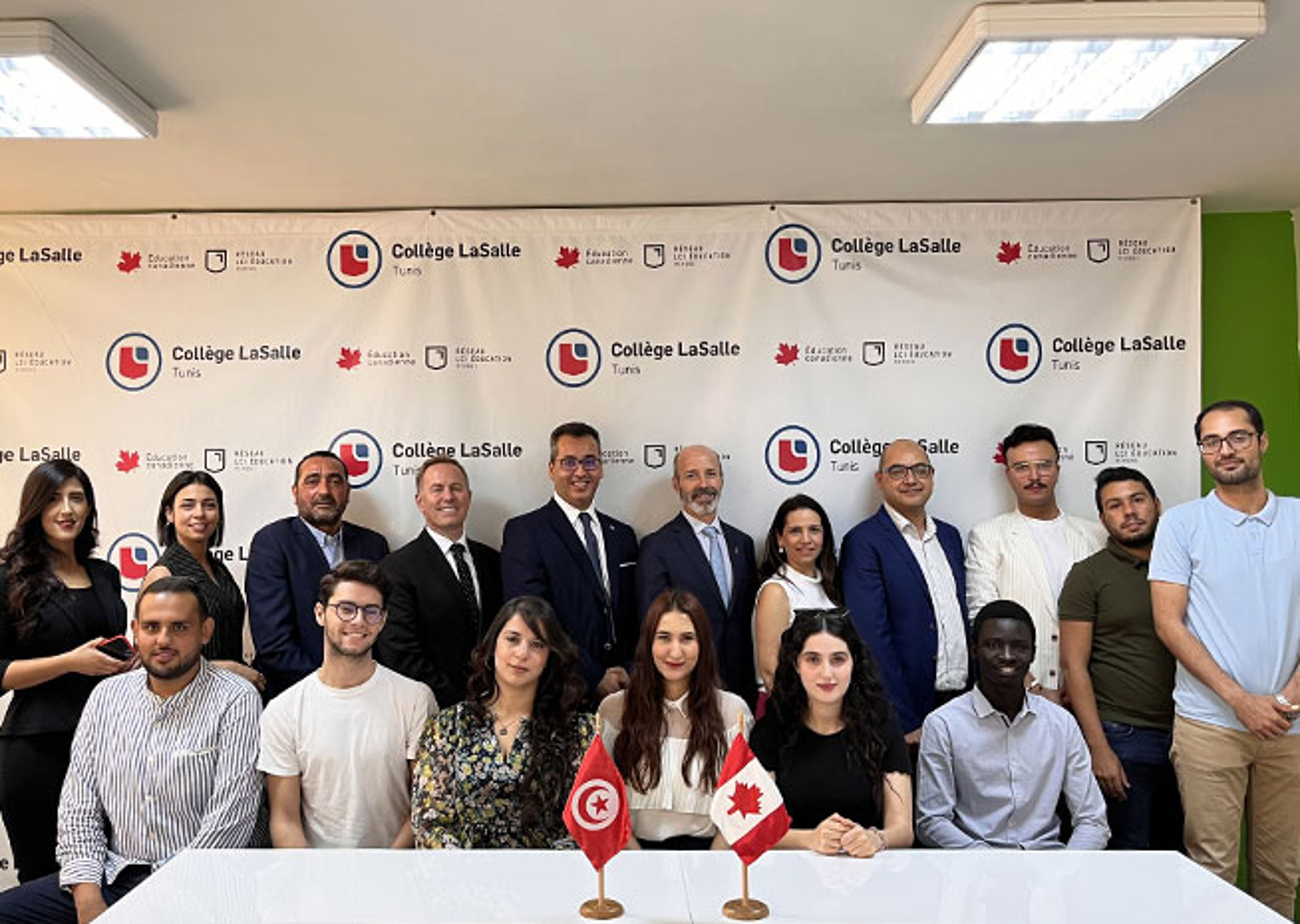 Un groupe diversifié se réunit pour une photo commémorative au Collège LaSalle de Tunis, avec des drapeaux tunisiens et canadiens sur la table, symbolisant un partenariat.