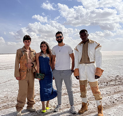 Quatre personnes élégantes posent avec assurance sur une vaste plaine de sel sous un ciel lumineux, exhibant des choix de mode divers et audacieux.
