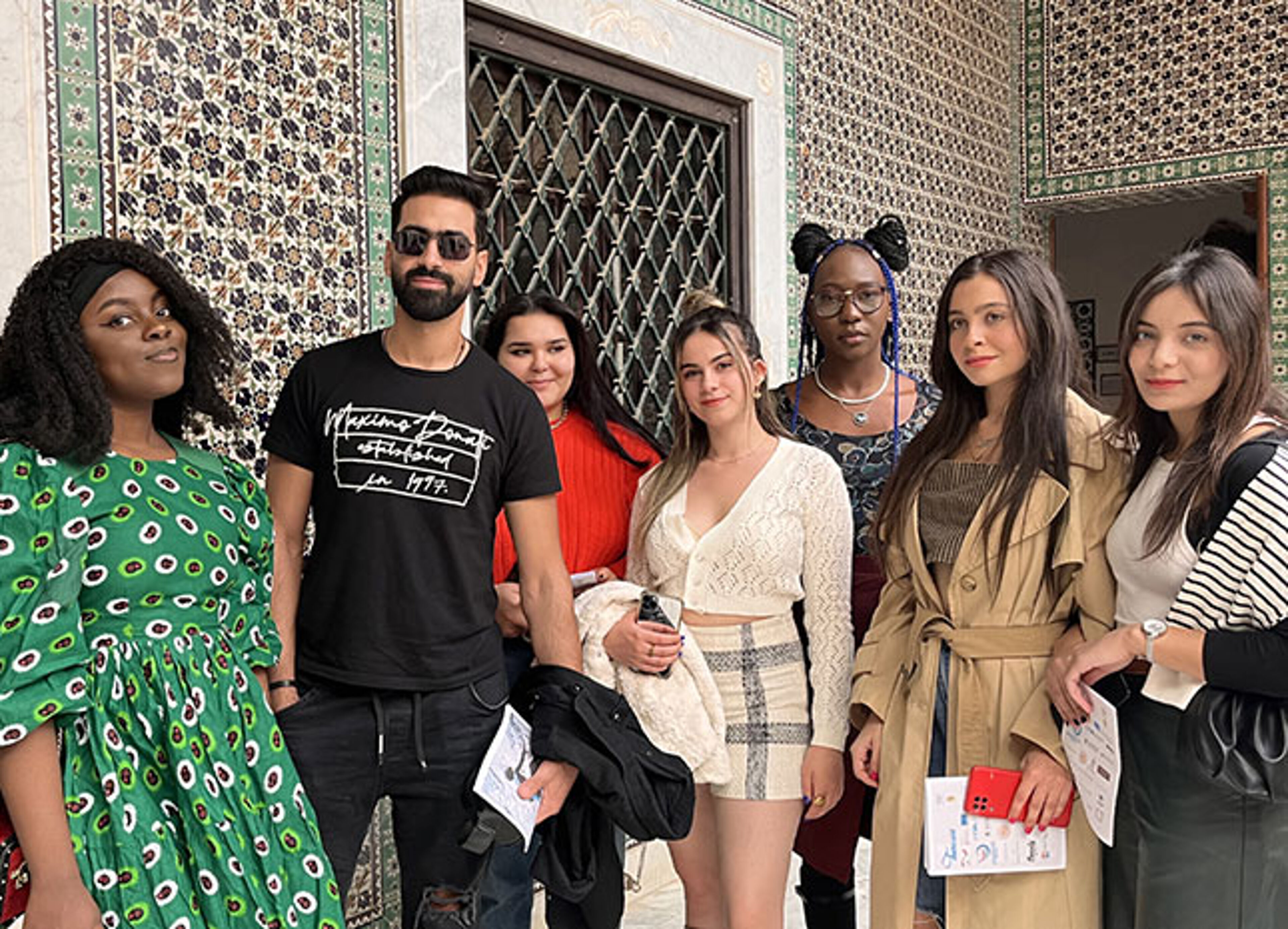 Un groupe de six personnes à la pointe de la mode pose ensemble devant une mosaïque traditionnelle, dégageant confiance et style.