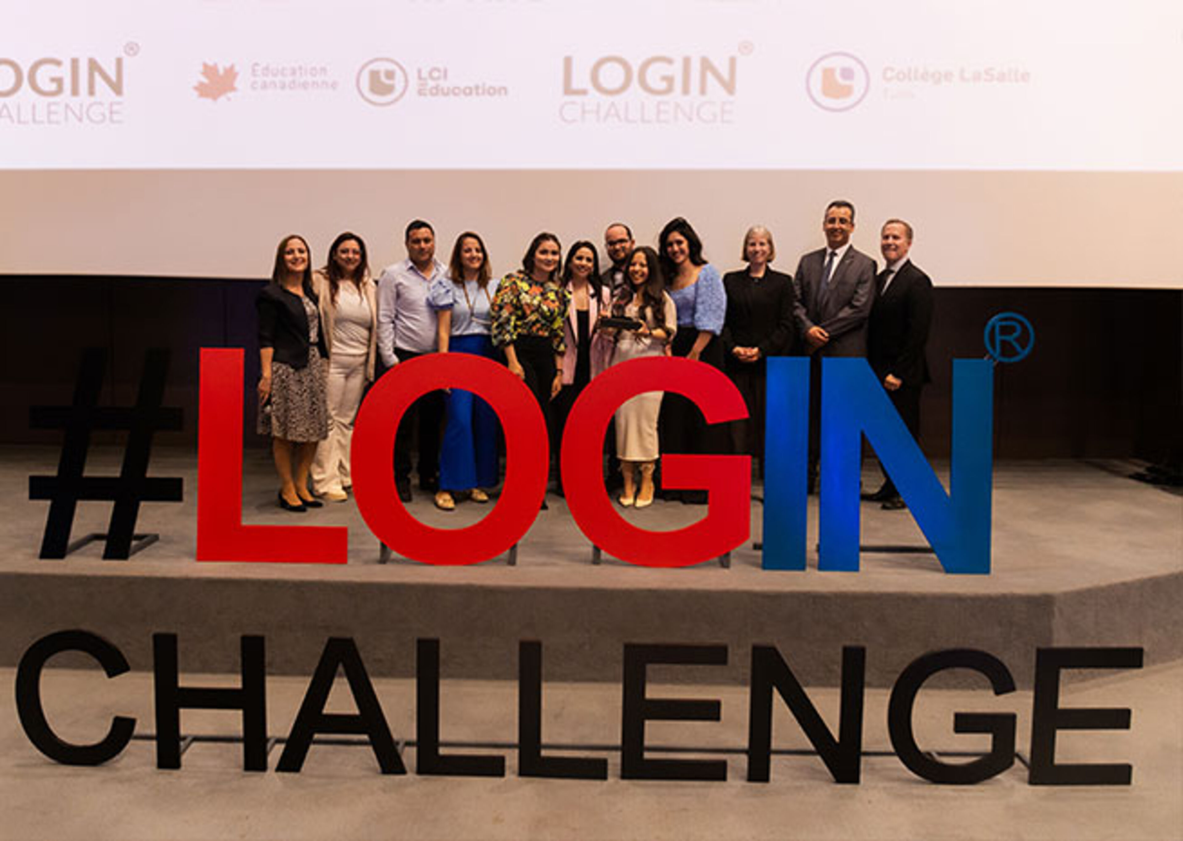 Un groupe varié pose devant un grand panneau "#LOGIN CHALLENGE" en rouge et bleu, probablement participants ou organisateurs d'un événement technologique ou éducatif.
