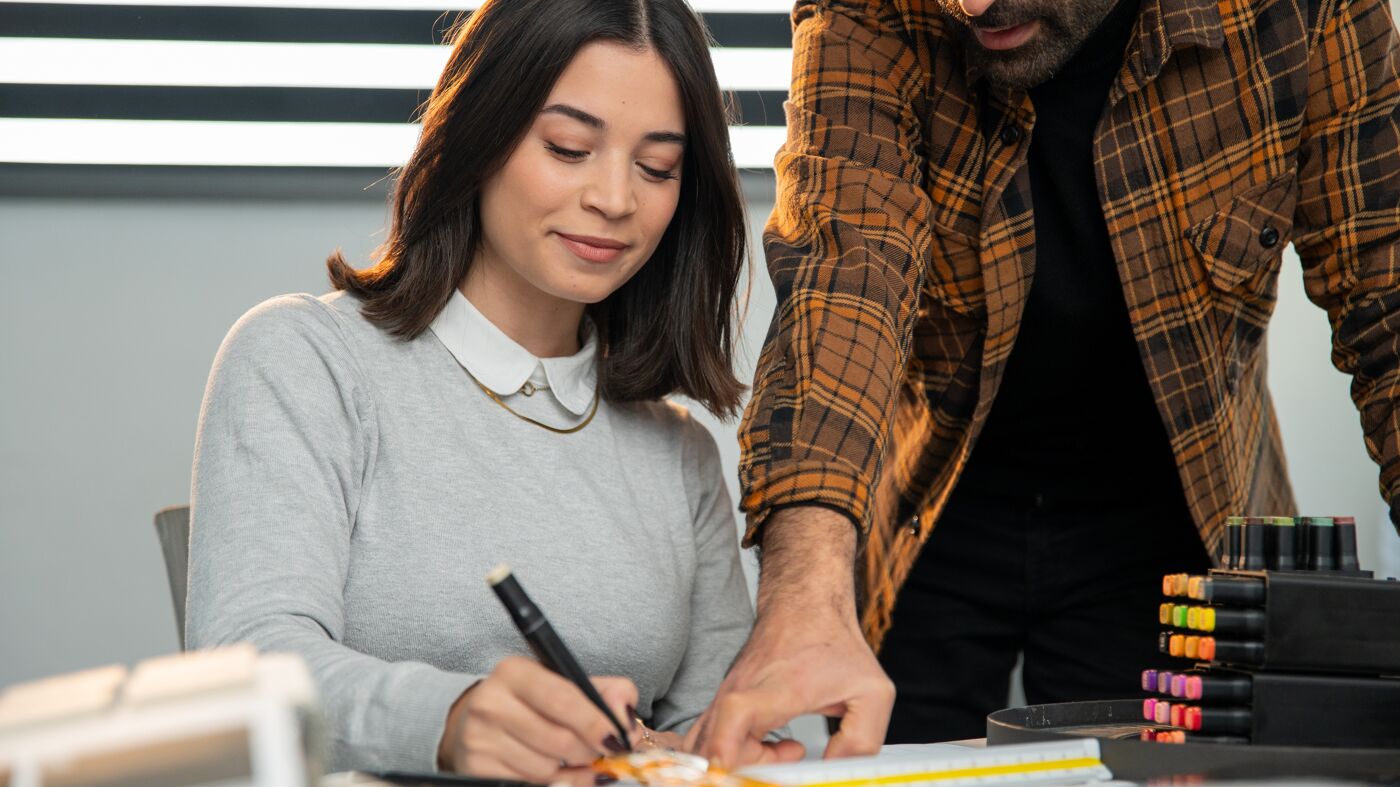 A woman and a man review documents in a modern office setting, with the focus on the woman annotating a paper.