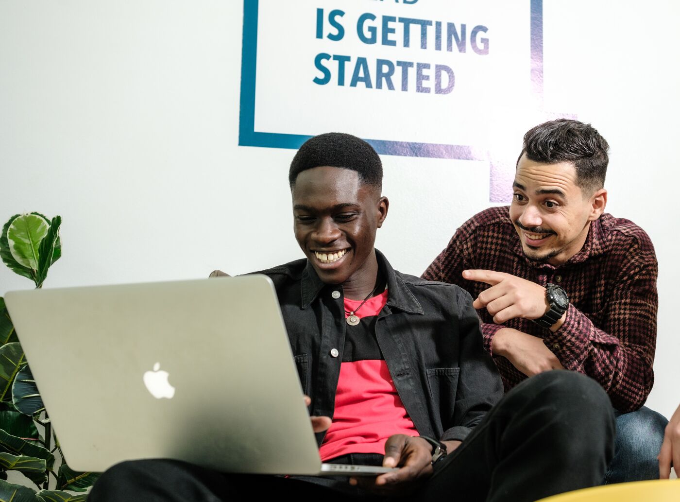 Three colleagues share a light moment around a laptop in an informal office setting.
