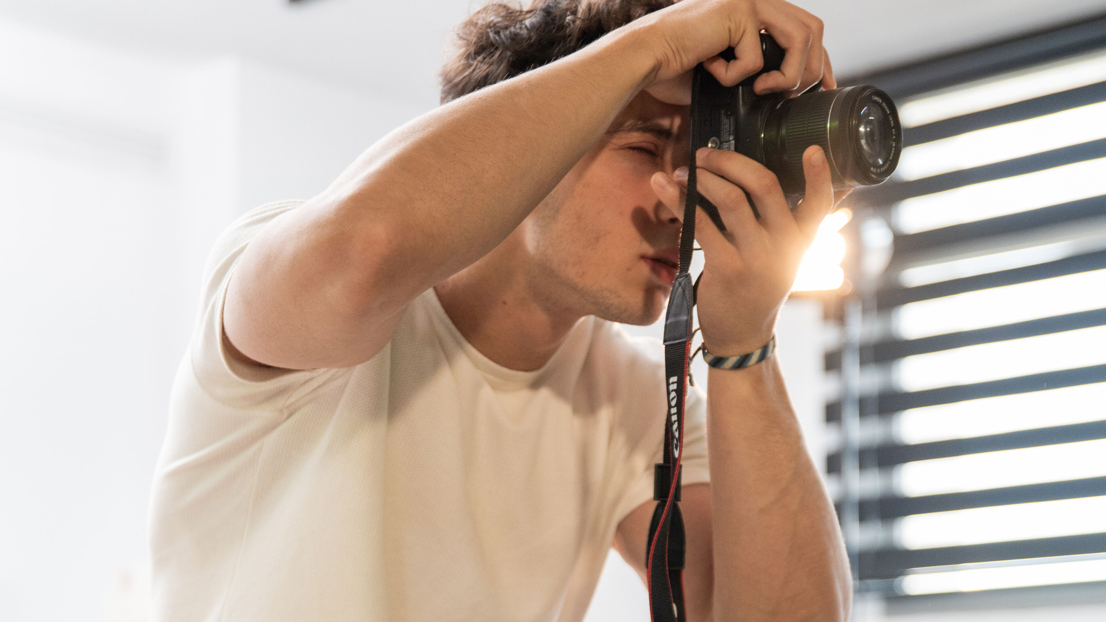Un jeune photographe se concentre intensément à travers le viseur d'un appareil photo reflex numérique.