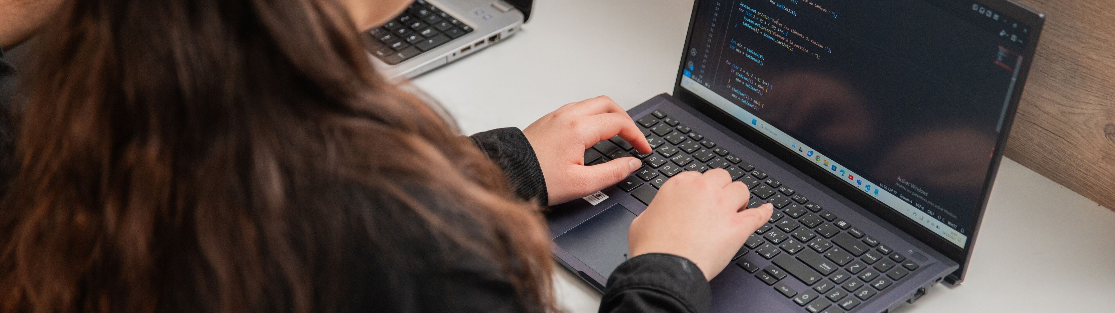 Une femme programme sur un ordinateur portable, le code est visible à l'écran.